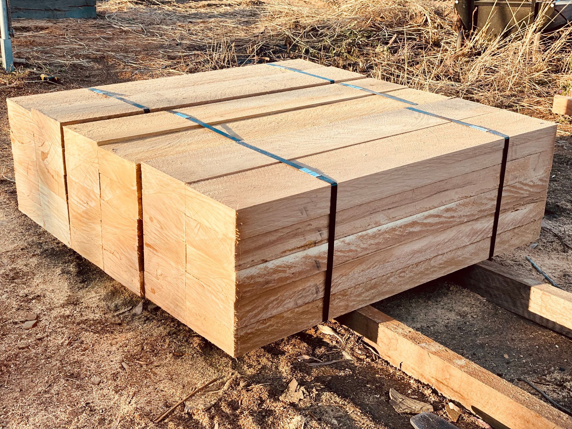 A stack of light-colored, sawn timber boards bound together with metal straps, resting on a wooden pallet outdoors. — LS Plant Hire in Calliope, QLD