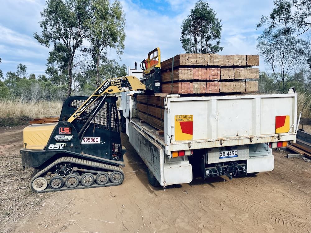 Mini Excavator Loading Wooden Beams Onto a White Truck in a Rural Setting — LS Plant Hire in Calliope, QLD
