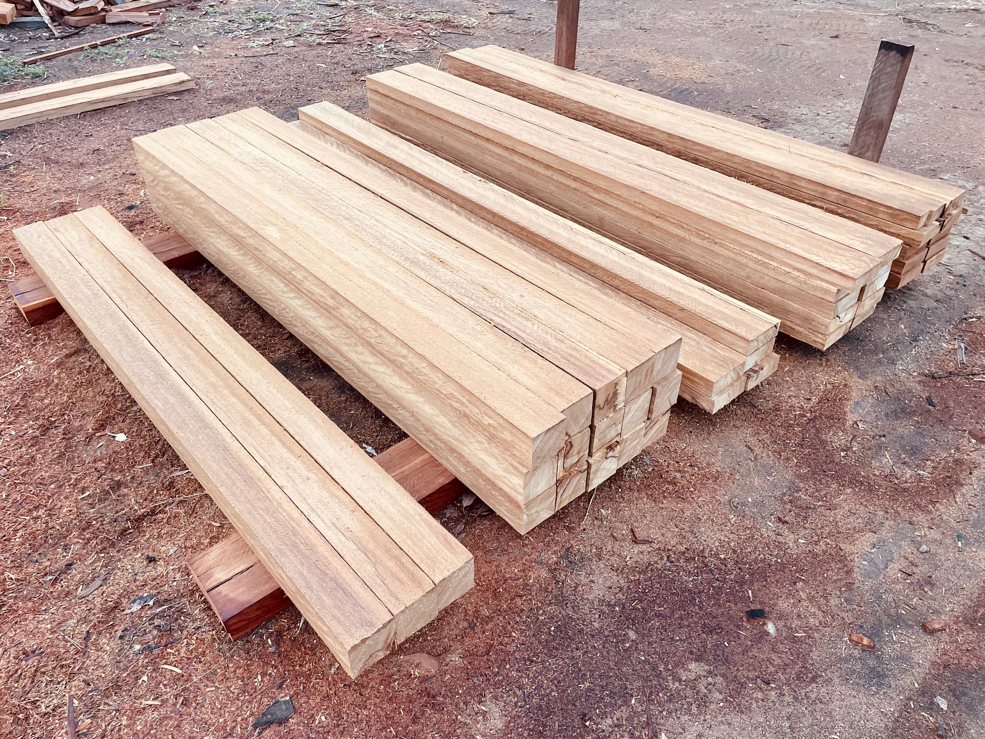 Stacks of light-colored, rectangular wooden beams resting on the ground in an outdoor workshop. — LS Plant Hire in Calliope, QLD