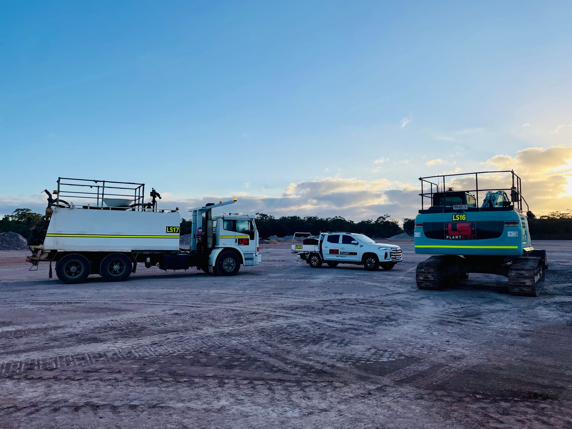 A service truck, pickup, and excavator parked on a dirt lot under a bright, sunny sky. — LS Plant Hire in Calliope, QLD