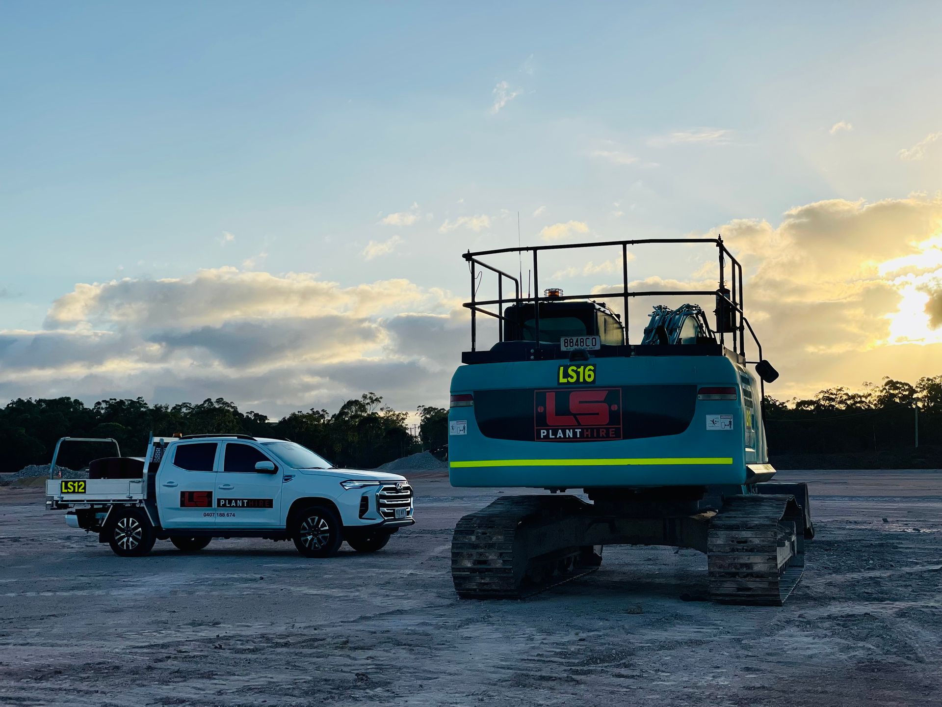 A white pickup truck parked next to a large, teal-colored excavator on a gravel lot under a sunrise sky. — LS Plant Hire in Calliope, QLD