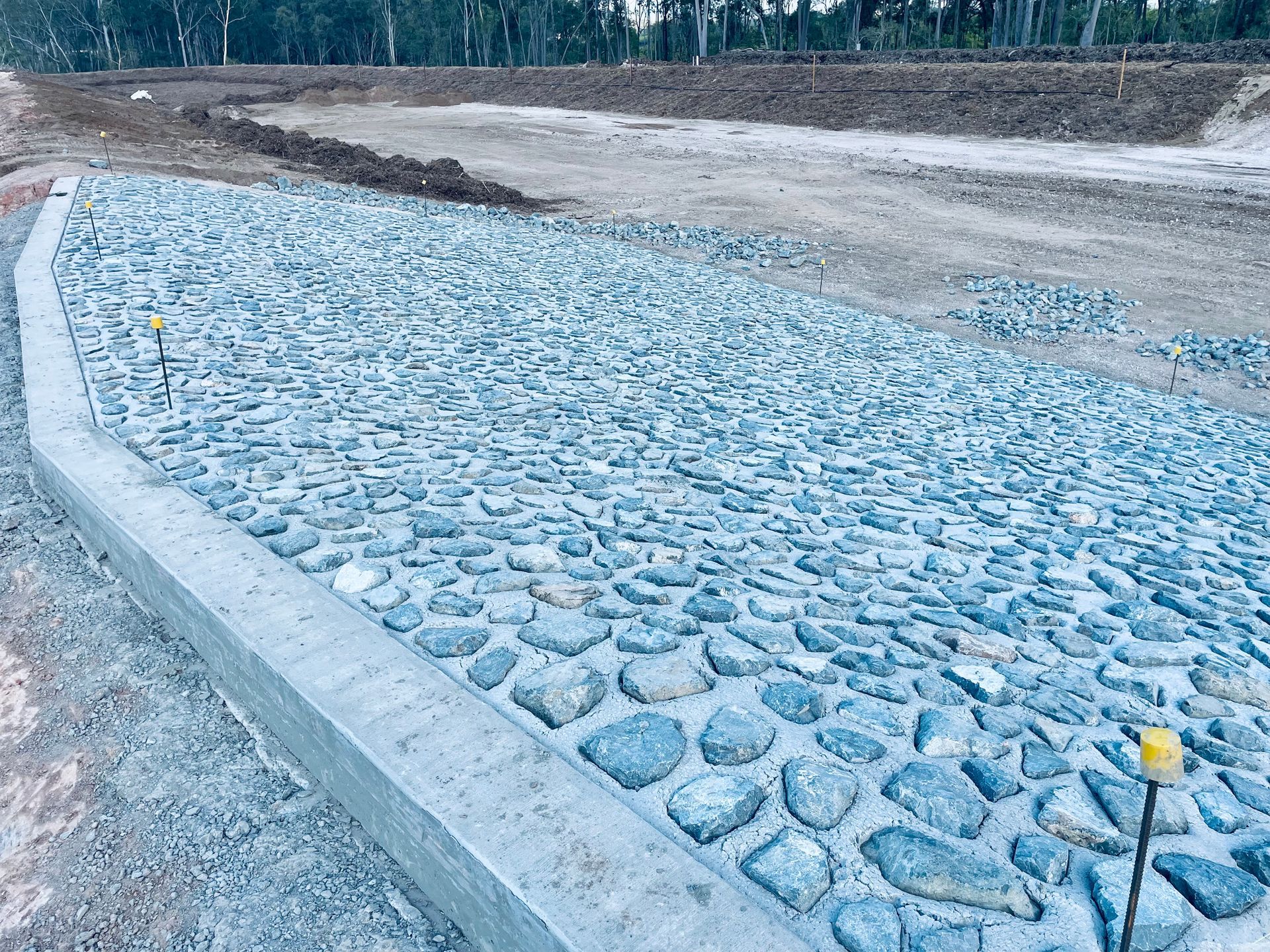 A concrete curb borders a large slope paved with grey cobblestones at a construction site. — LS Plant Hire in Calliope, QLD