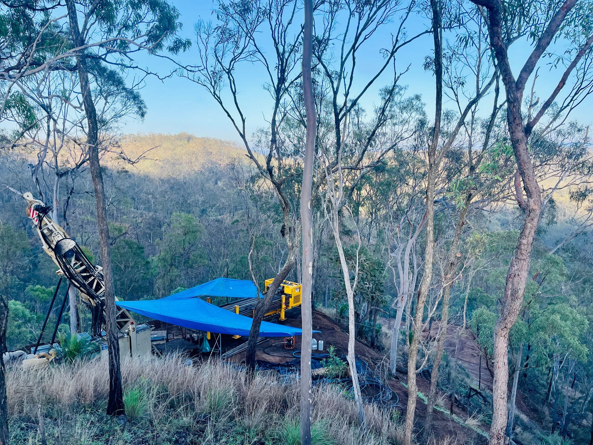 A drilling rig and blue tarps set up on a hillside in a sparse, dry forest clearing. — LS Plant Hire in Calliope, QLD
