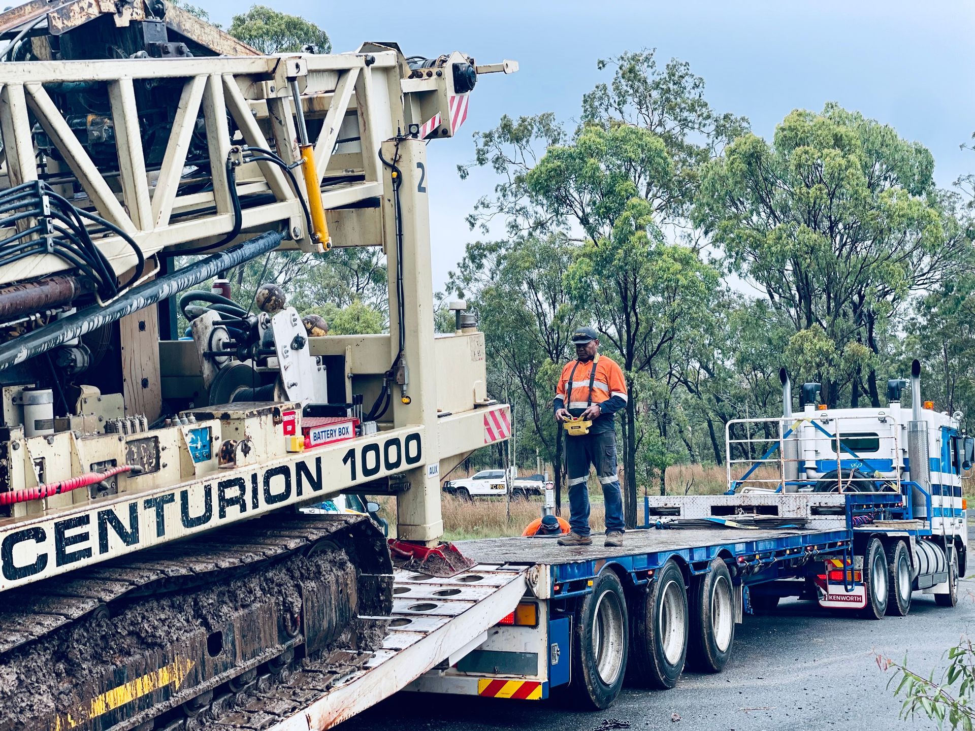 A worker in orange high-vis gear operates a drill rig labeled 