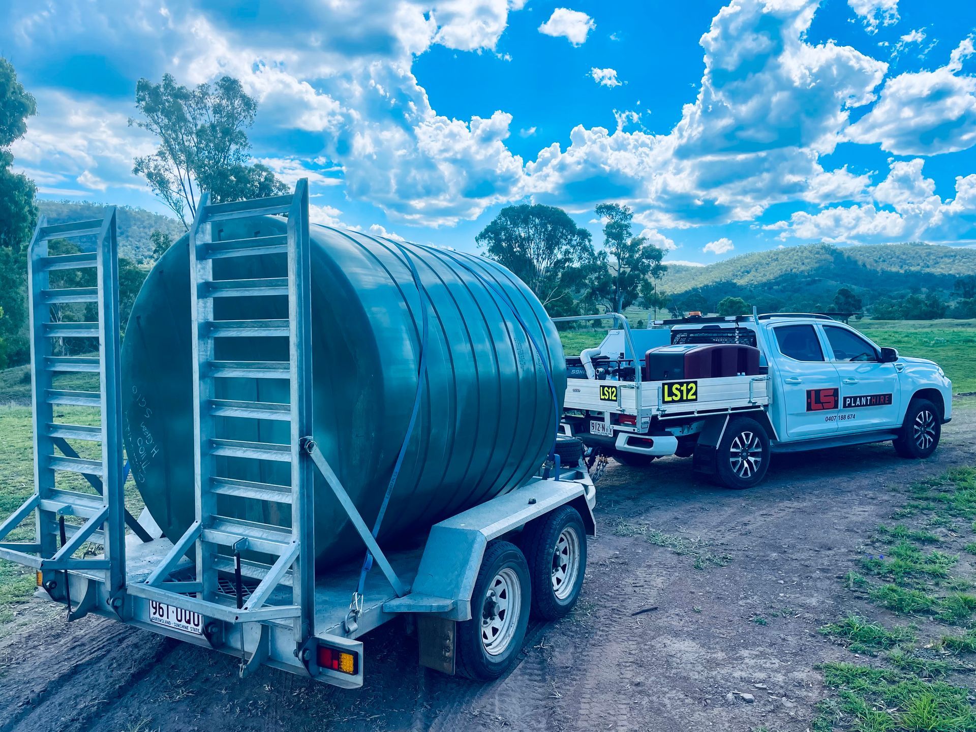 A white pickup truck towing a flatbed trailer with a large, cylindrical green water tank on a rural dirt path. — LS Plant Hire in Calliope, QLD