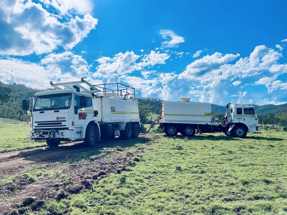 Two Water Trucks on a Grassy Field Under a Blue Sky With Clouds — LS Plant Hire in Calliope, QLD