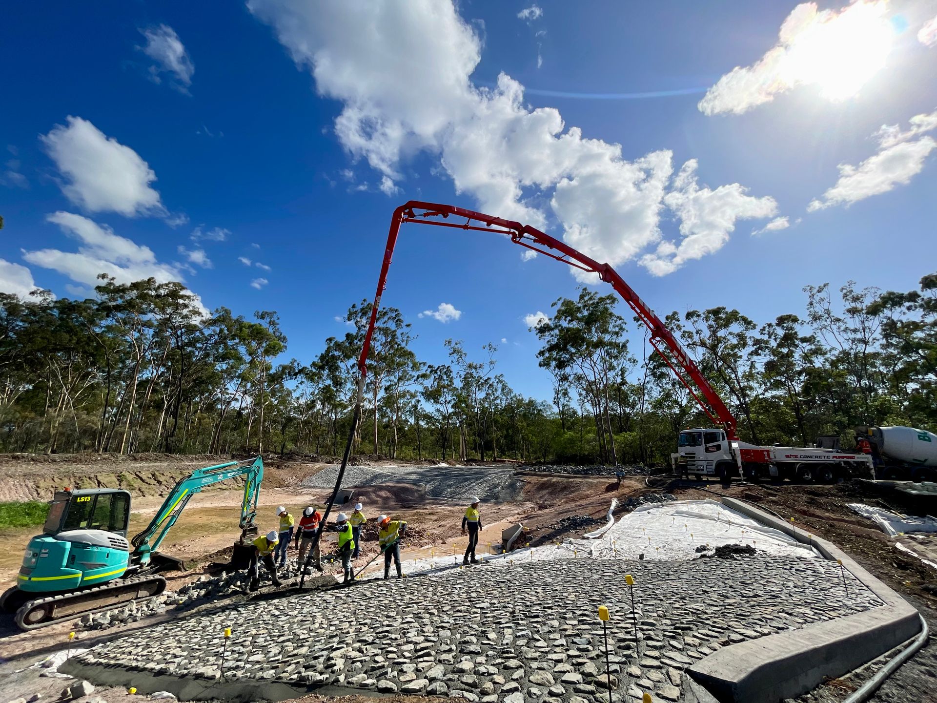 Workers operate a concrete pump truck at a construction site, pouring concrete over a rock-filled base near trees. — LS Plant Hire in Calliope, QLD