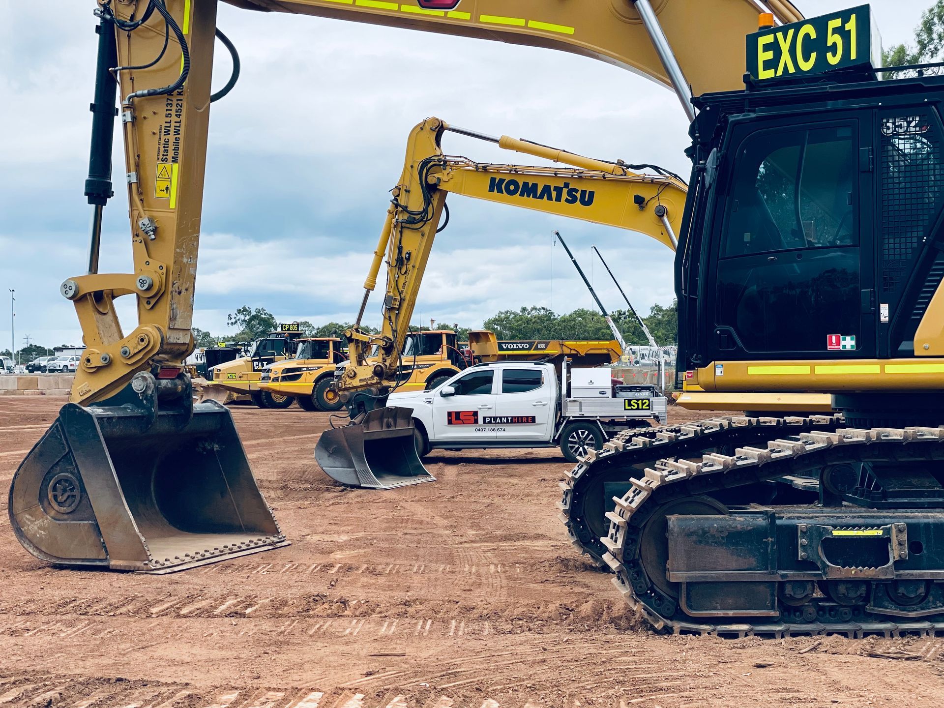 Two yellow construction excavators parked on a dirt lot, with a white pickup truck between them under a cloudy sky. — LS Plant Hire in Calliope, QLD