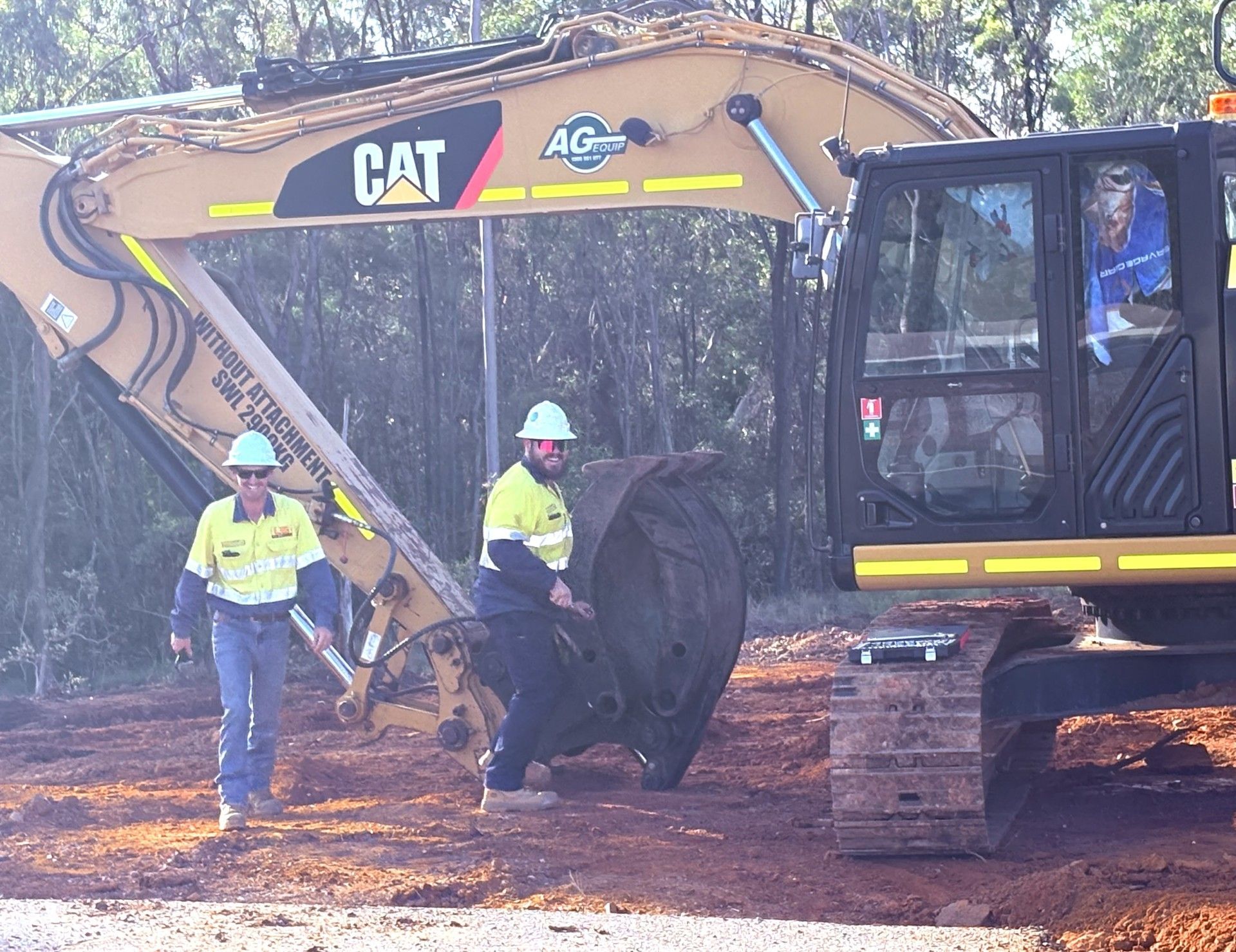 Two workers in high-visibility clothing stand next to a large yellow CAT excavator on a dirt construction site. — LS Plant Hire in Calliope, QLD