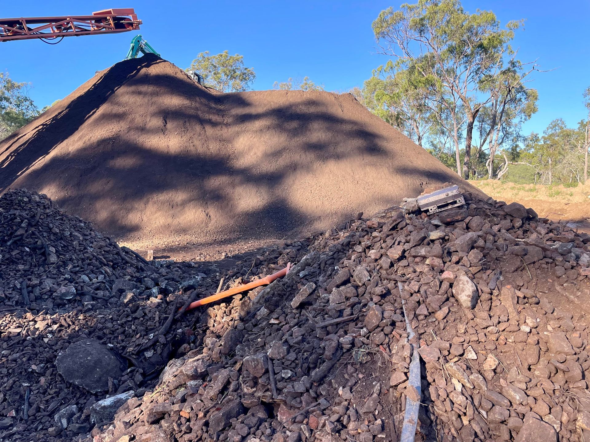 A large pile of dirt and rocks at a construction or mining site under a clear blue sky. — LS Plant Hire in Calliope, QLD