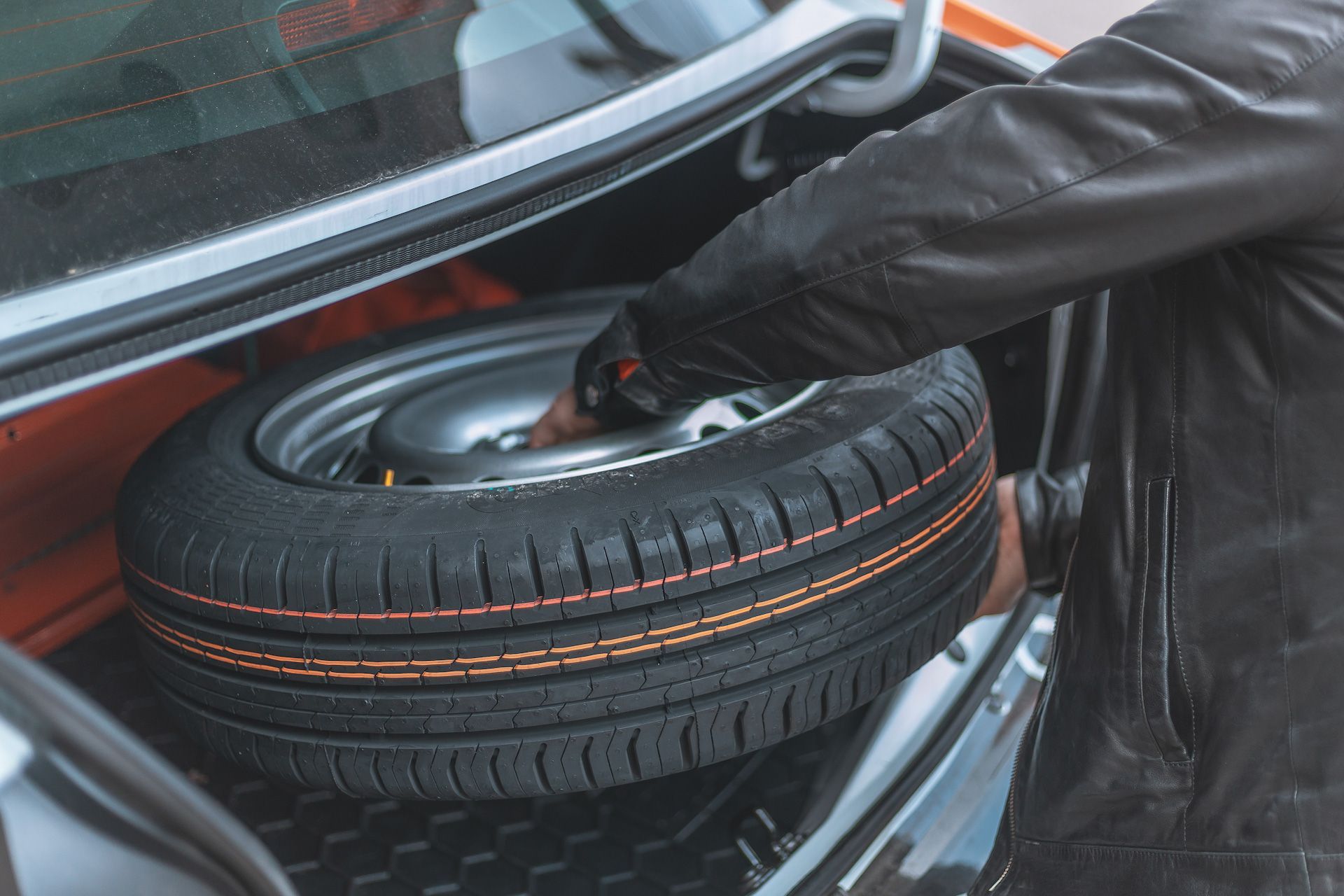 A person is putting a spare tire in the trunk of a car.