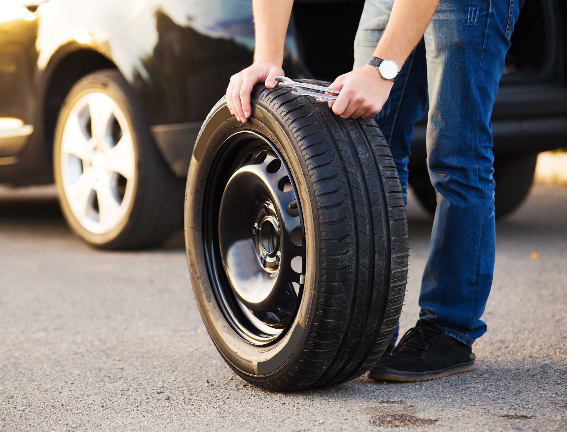 A person is holding a tire in front of a car.
