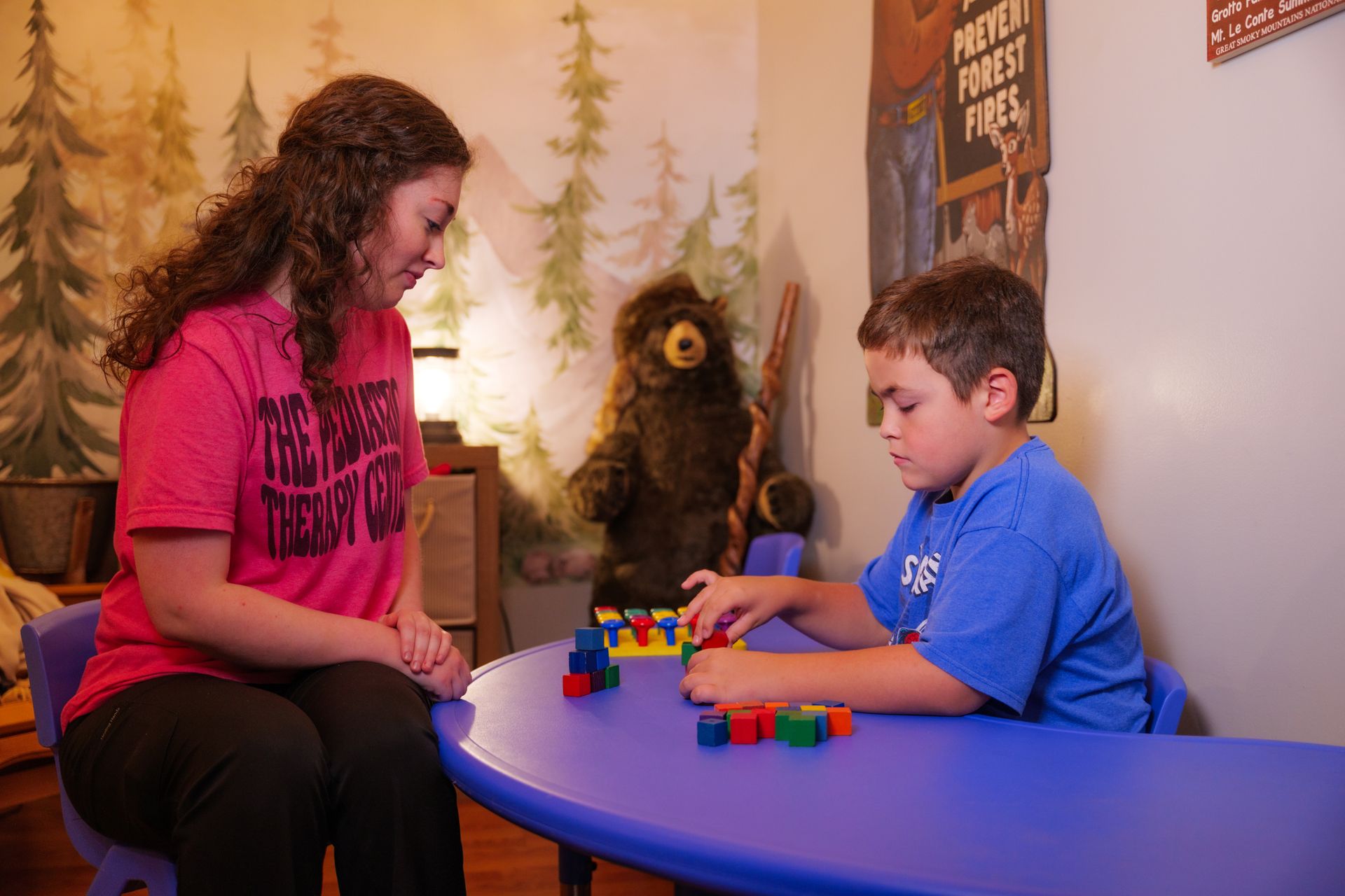 A woman is sitting at a table with a boy playing with blocks.