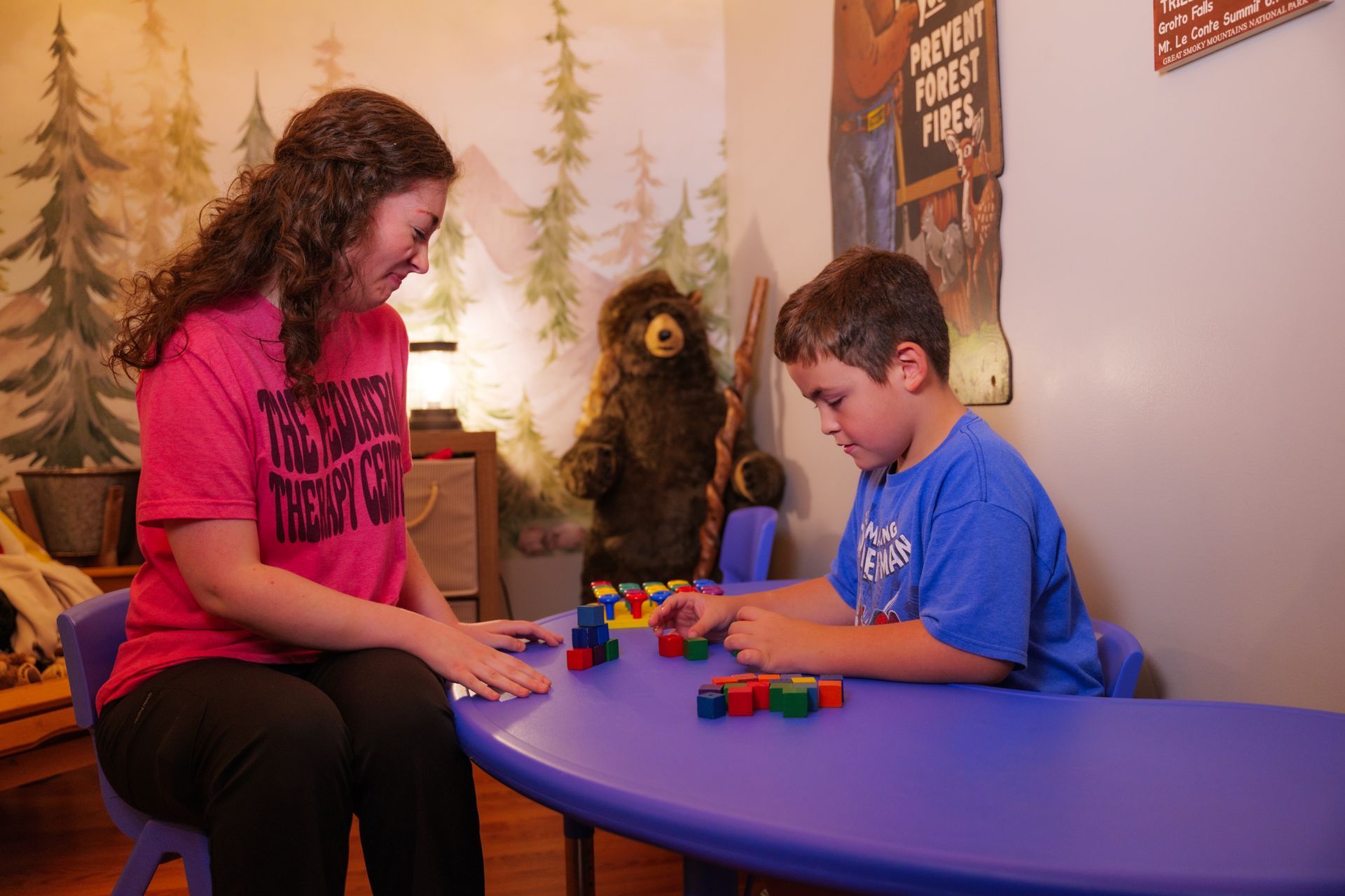 A woman is sitting at a table with a boy playing with blocks.