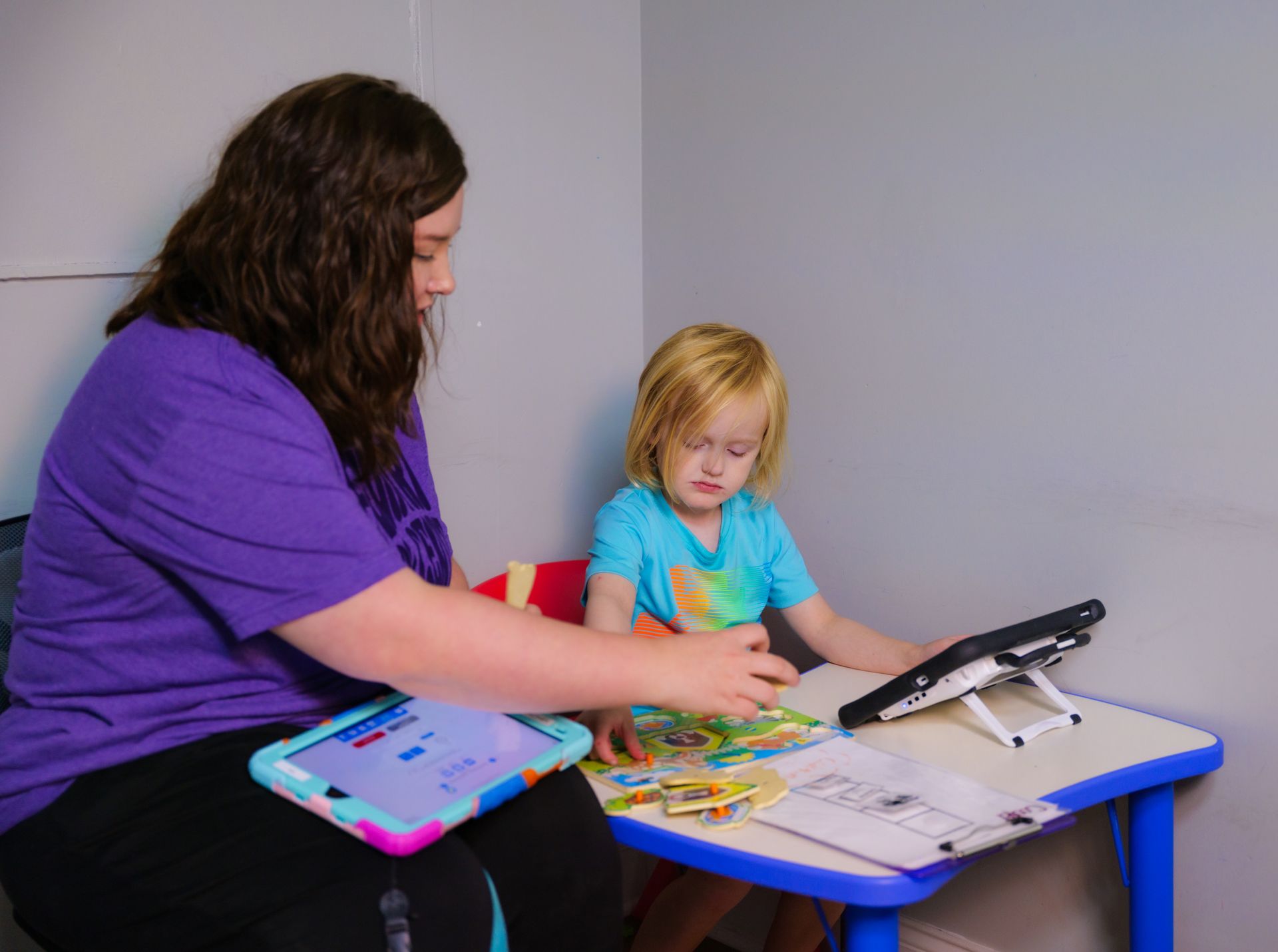 A woman is sitting at a table with a child using a tablet.