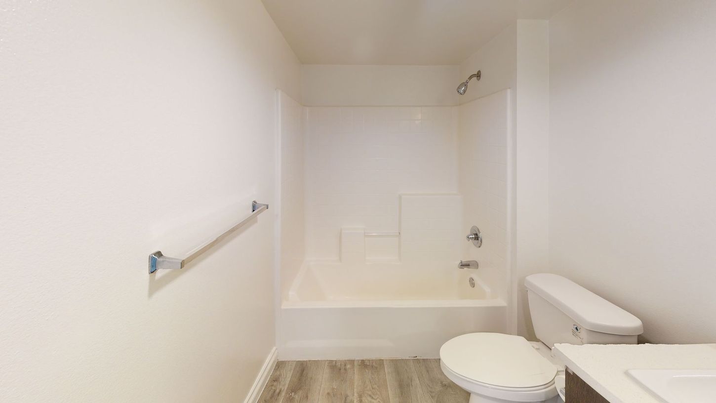 Bathroom with white walls, tub/shower, toilet, and towel rack. Light wood-look flooring.