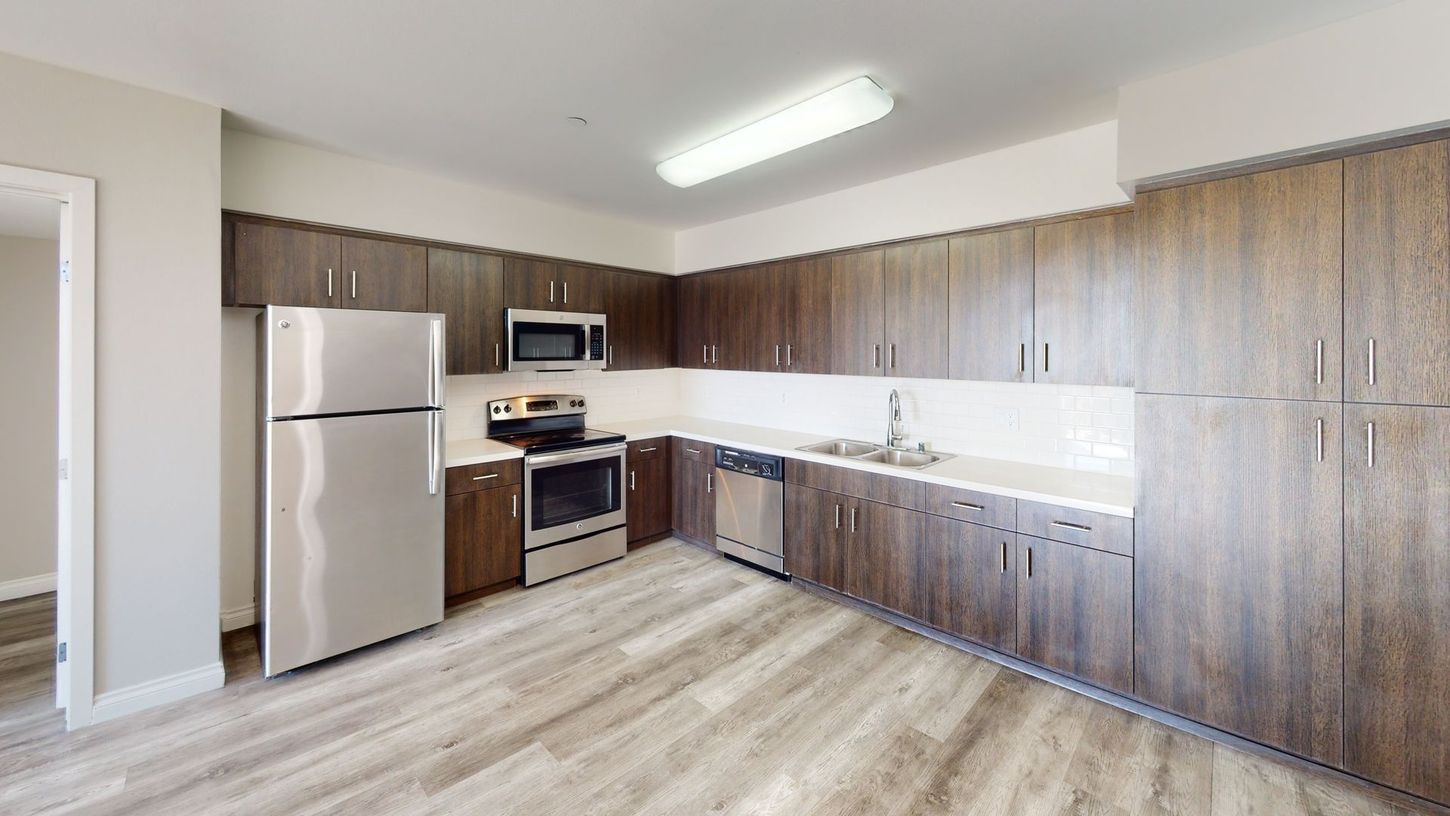 Kitchen with stainless steel appliances, brown cabinets, white countertops, and wood-look flooring.