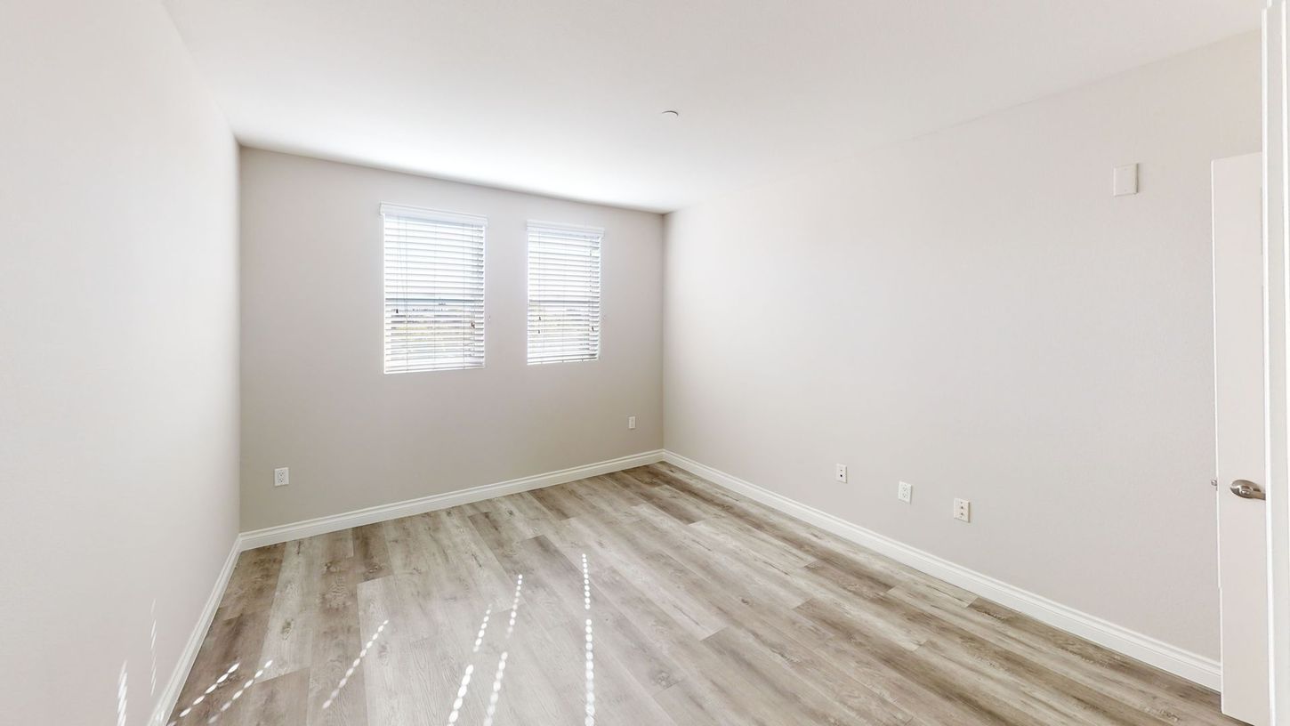 Empty room with light gray walls, two windows, and wood-look flooring.