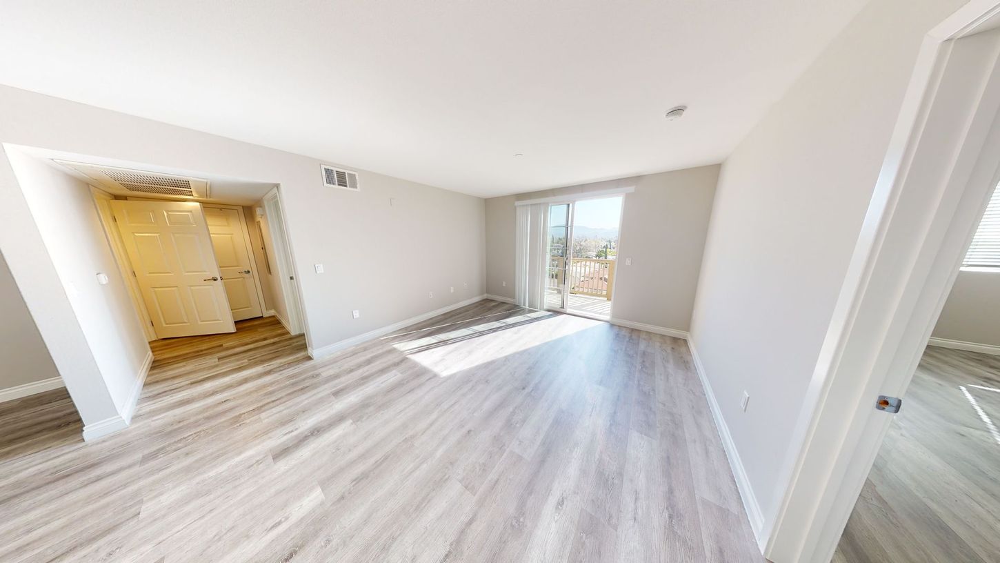 Empty room with light gray wood-look flooring, white walls, and a glass door leading to a balcony.