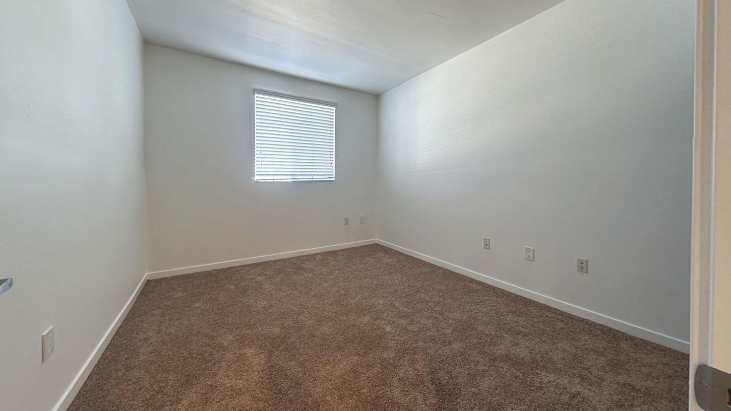 Empty room with brown carpet, white walls, and a window with blinds.