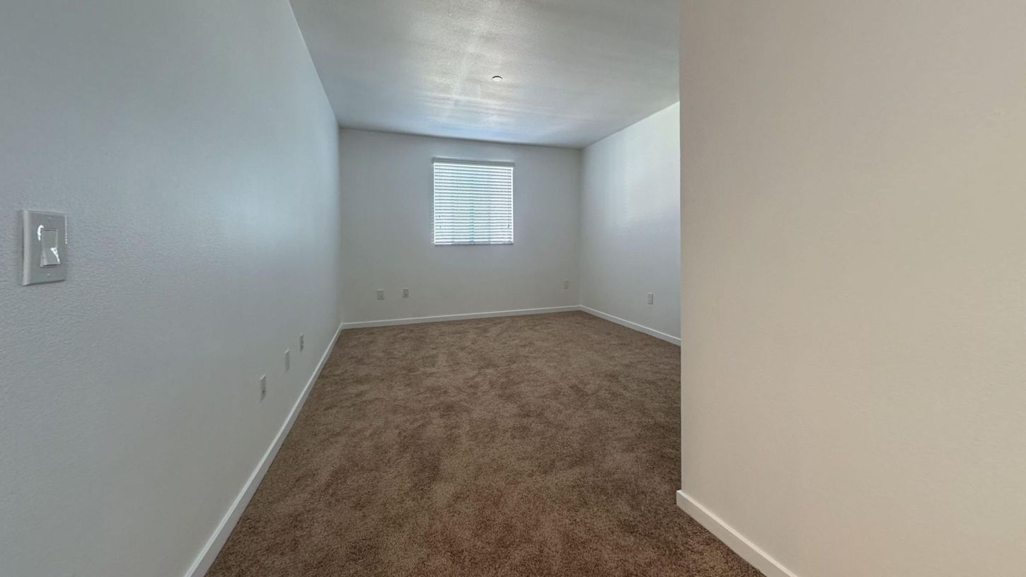 Empty room with brown carpet, window with blinds, and light-colored walls.