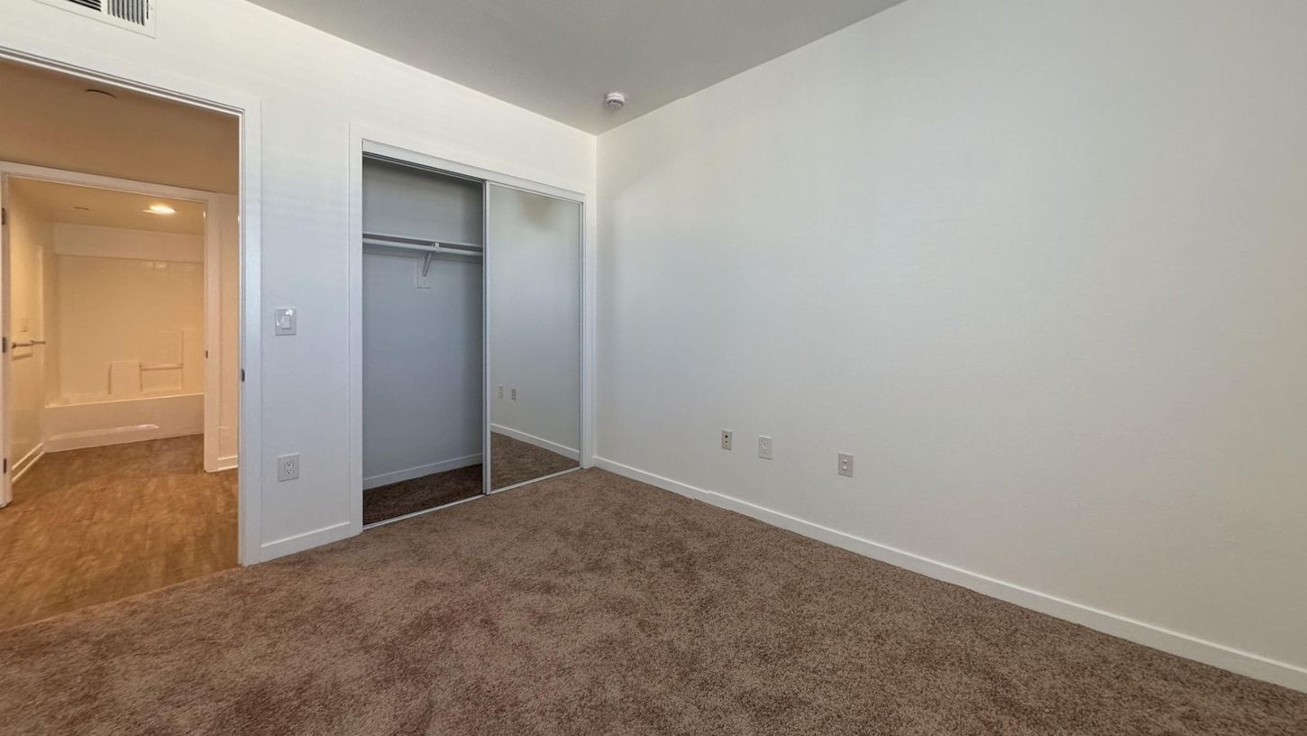 Bedroom with carpet, closet, and doorway to a bathroom. Beige walls and light.