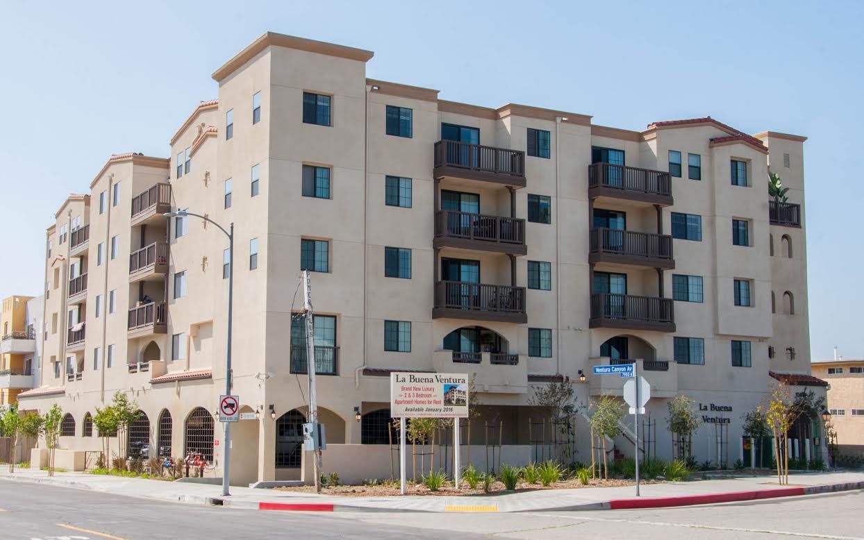 Multi-story apartment building, light beige stucco exterior, balconies, blue sky.