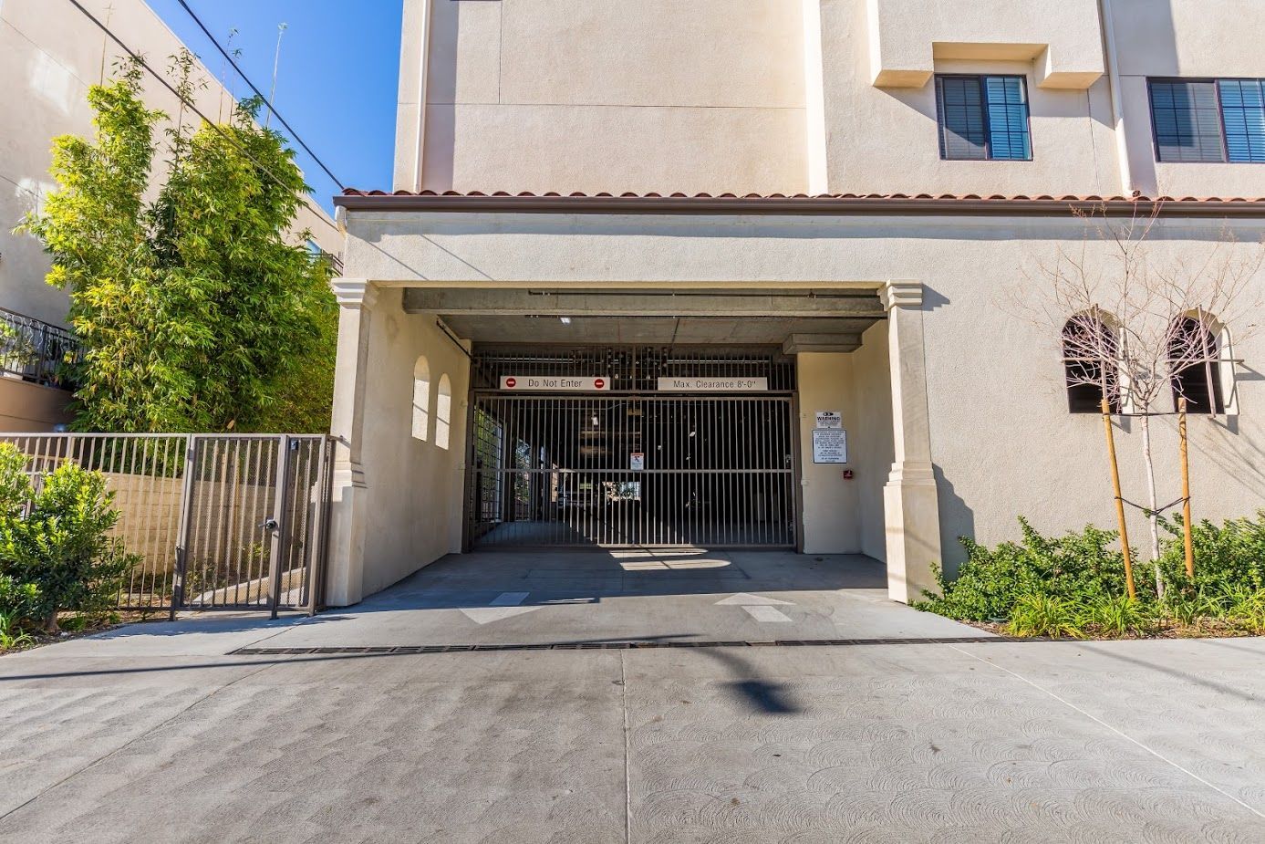 Entrance to a beige building with a small canopy over a glass door, surrounded by greenery.