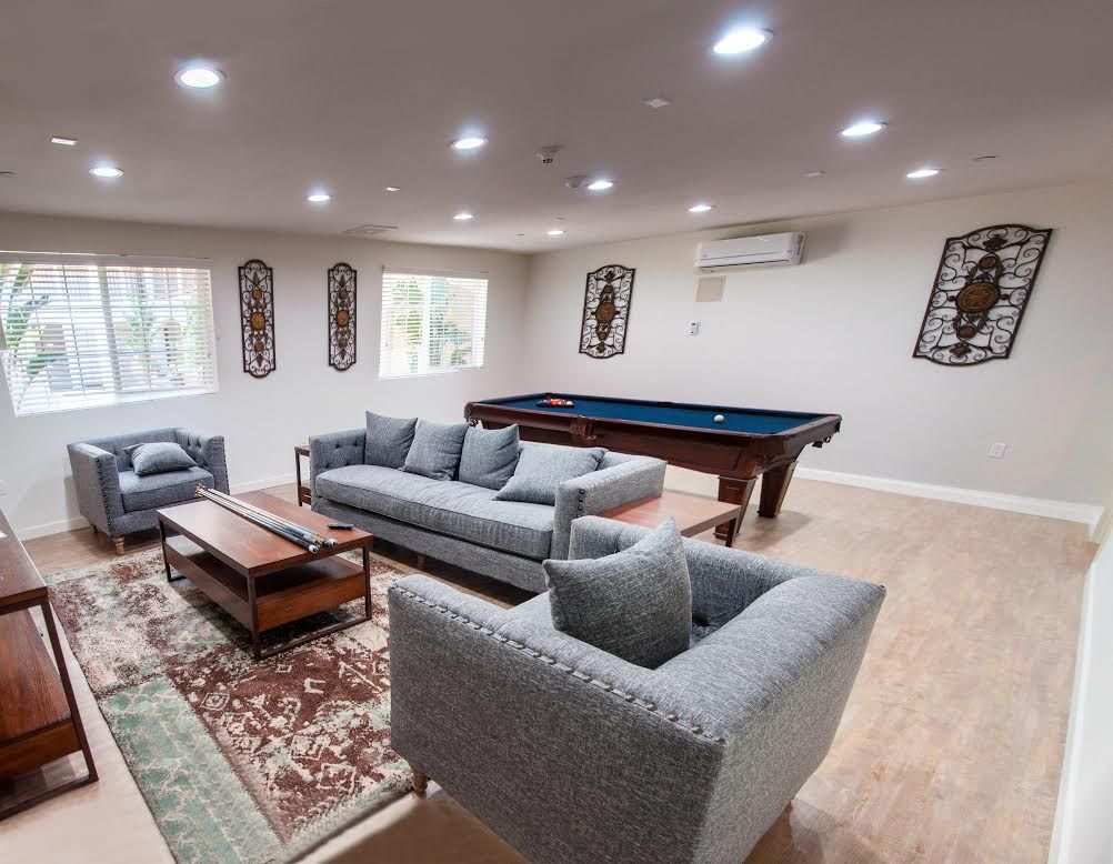Spacious game room with a pool table, gray sofas, and decorative wall art.
