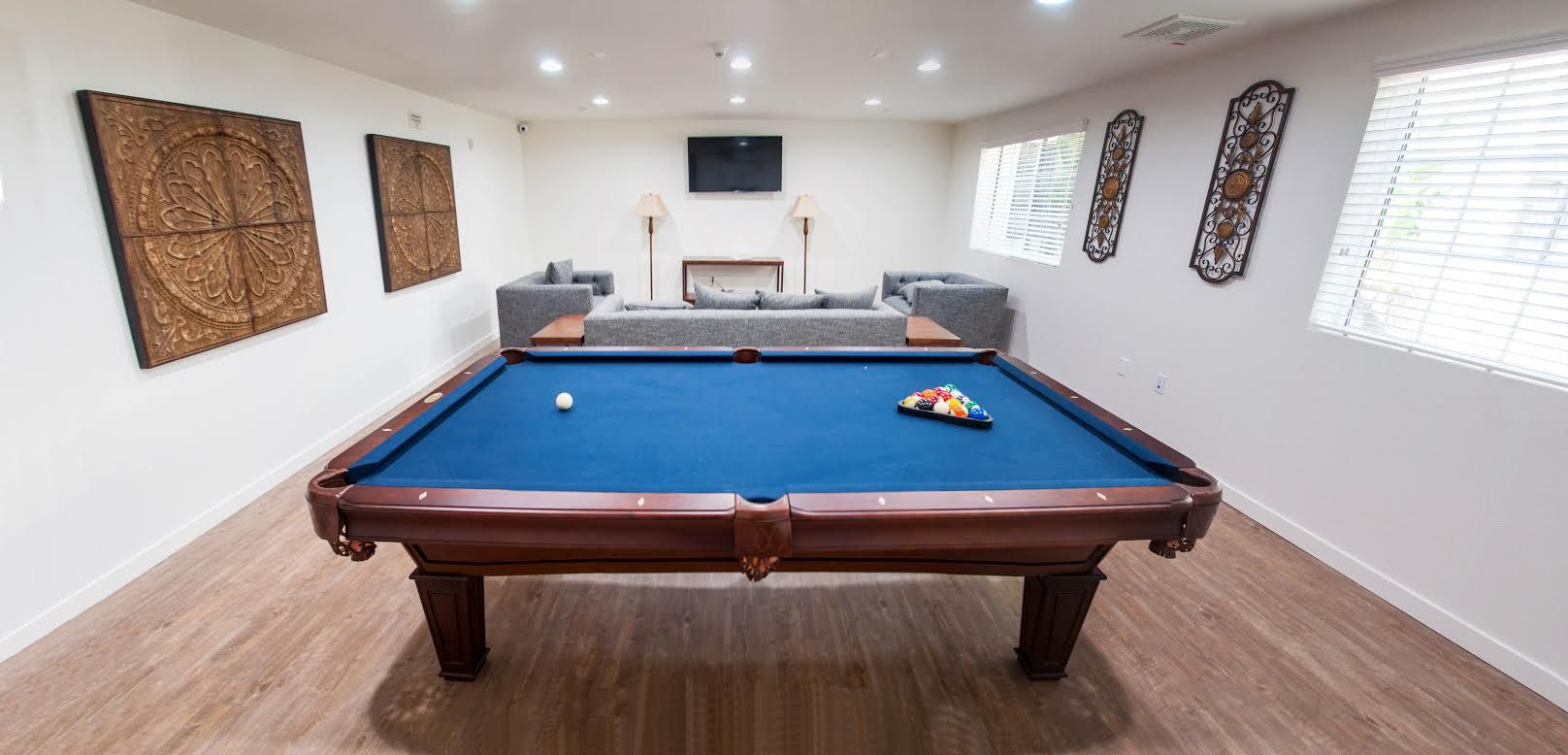 Pool table in a room with a seating area, wall art, and a TV. The table is blue and wooden.