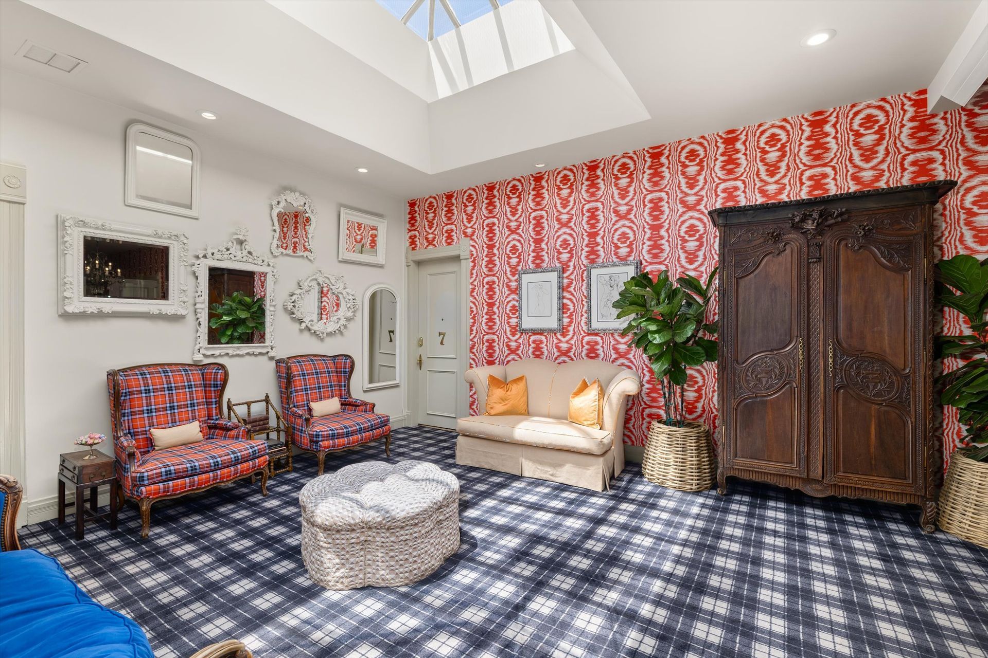 A room with red patterned wallpaper, plaid carpet, and ornate furniture, including a wooden armoire and patterned armchairs.