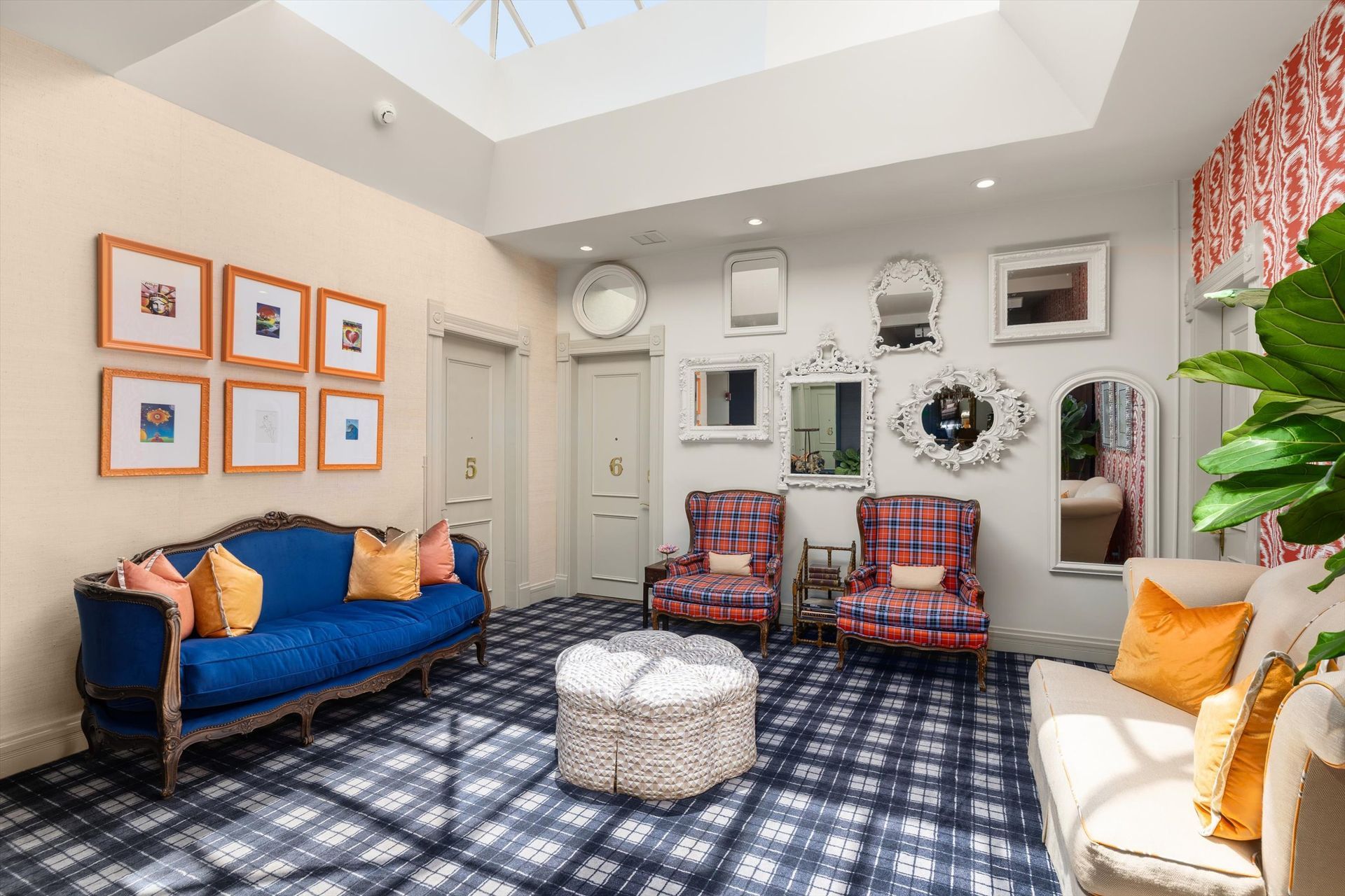 Cozy interior with blue sofa, plaid chairs, and a variety of mirrors on the wall. The room has a skylight and a patterned rug.