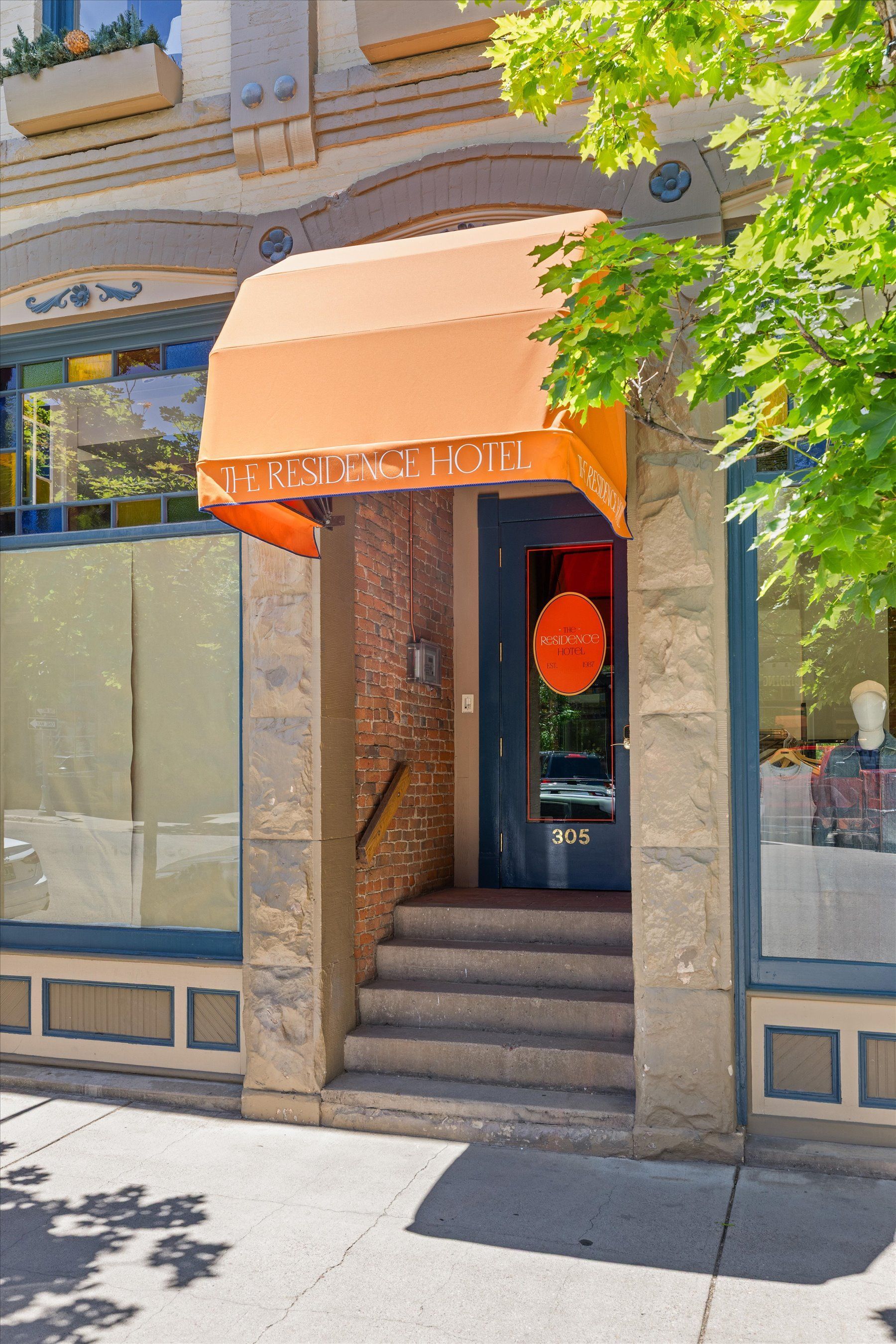 Entrance to the Residence Hotel with an orange awning and steps leading up to a blue door. Brickwork frames the entrance.