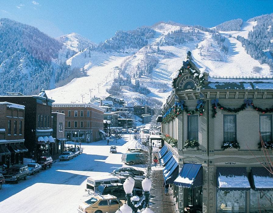 Snow-covered street in Aspen, Colorado, with historic buildings and a ski mountain in the background on a sunny day.