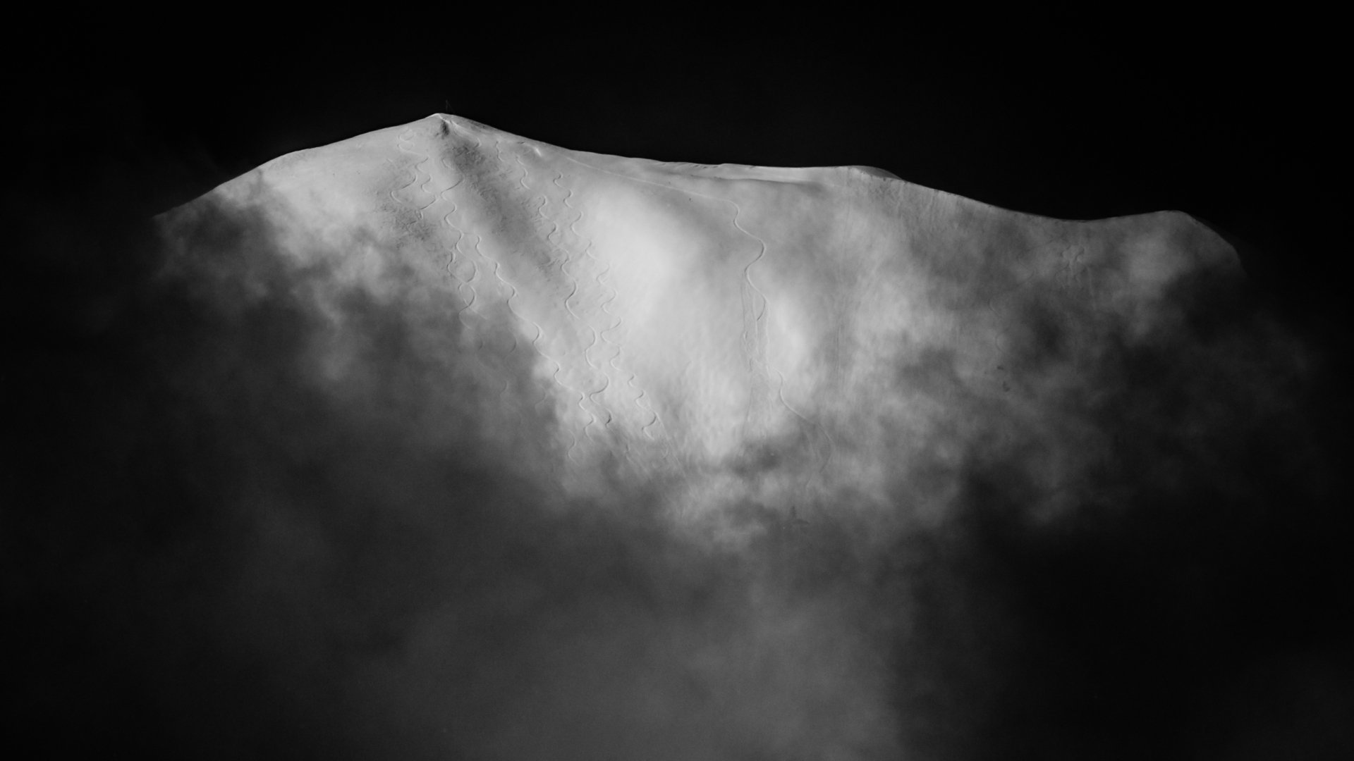 A black and white photo of Highlands Bowl covered in mist, with a dark background.