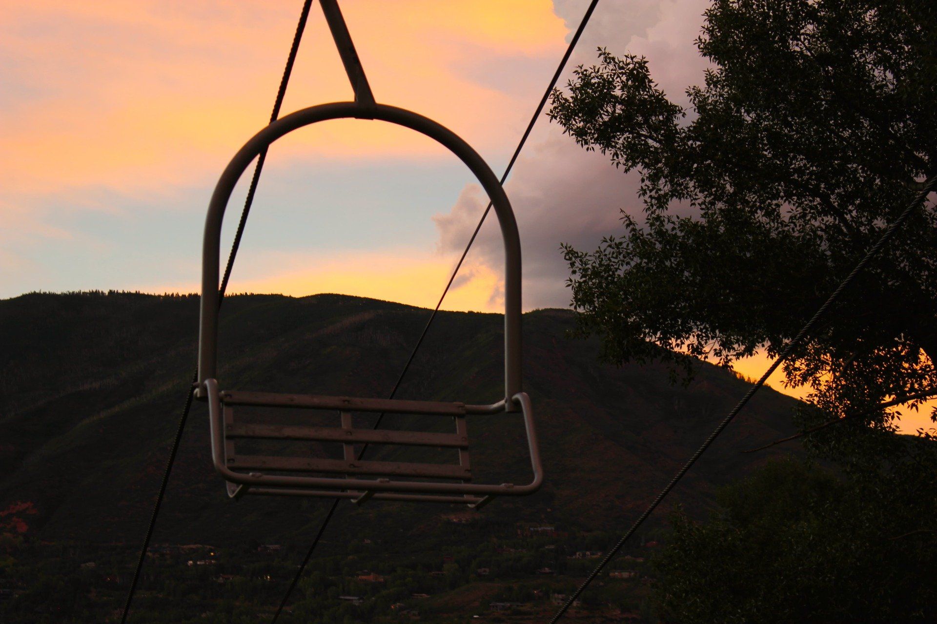 Empty ski lift chair silhouetted against a colorful sunset over a mountain range.