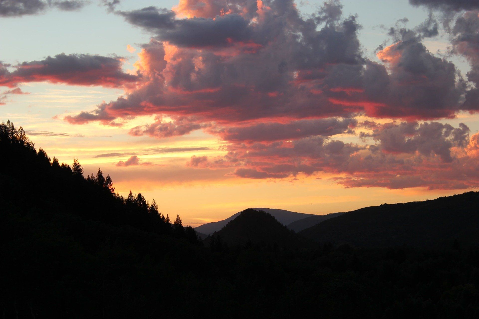 Sunset over a mountainous landscape with silhouetted hills and vibrant pink and orange clouds.