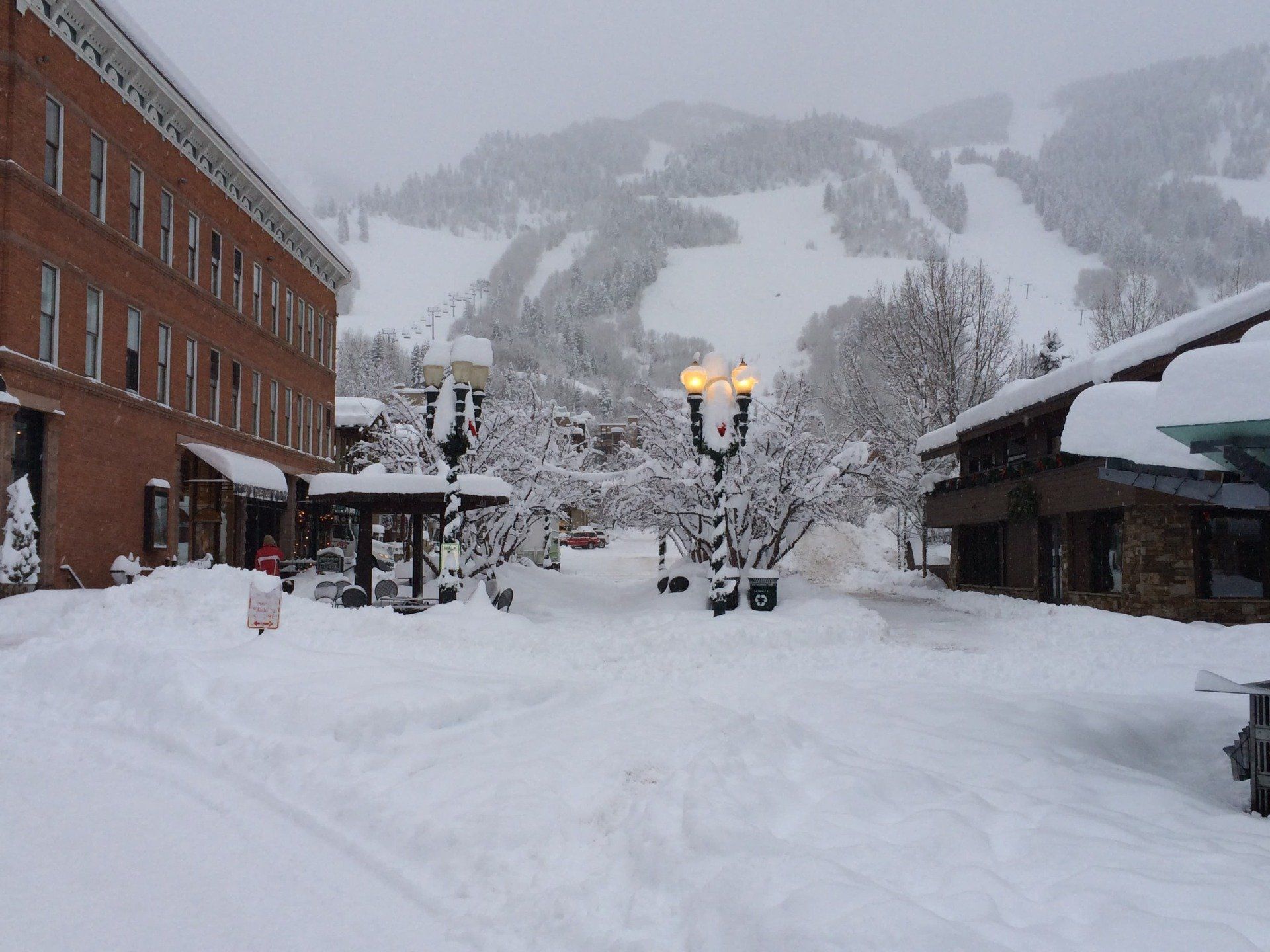 Snow-covered street in Aspen downtown with brick buildings and a ski slope in the background.