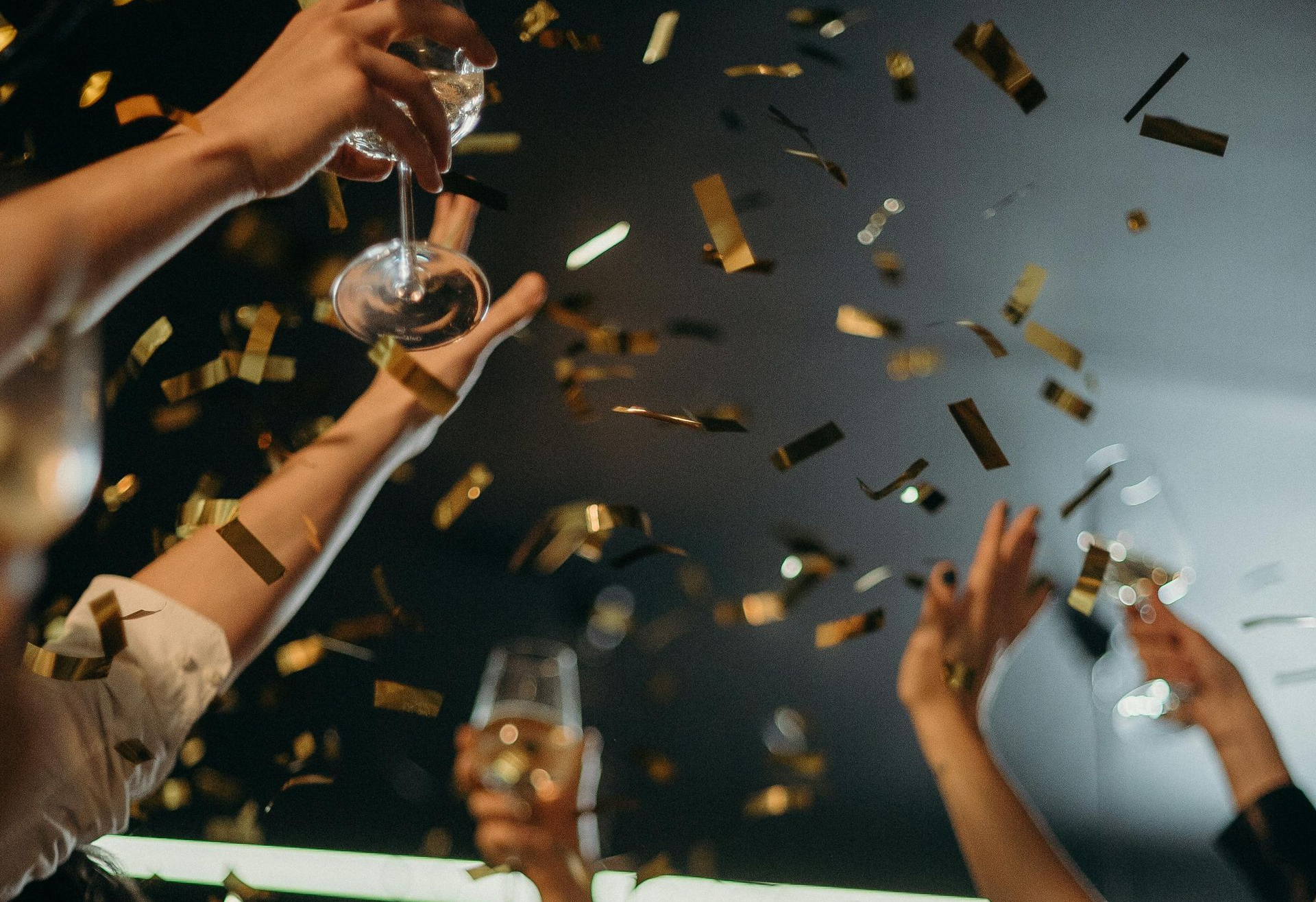 People celebrating, arms raised, confetti falling, glasses raised.