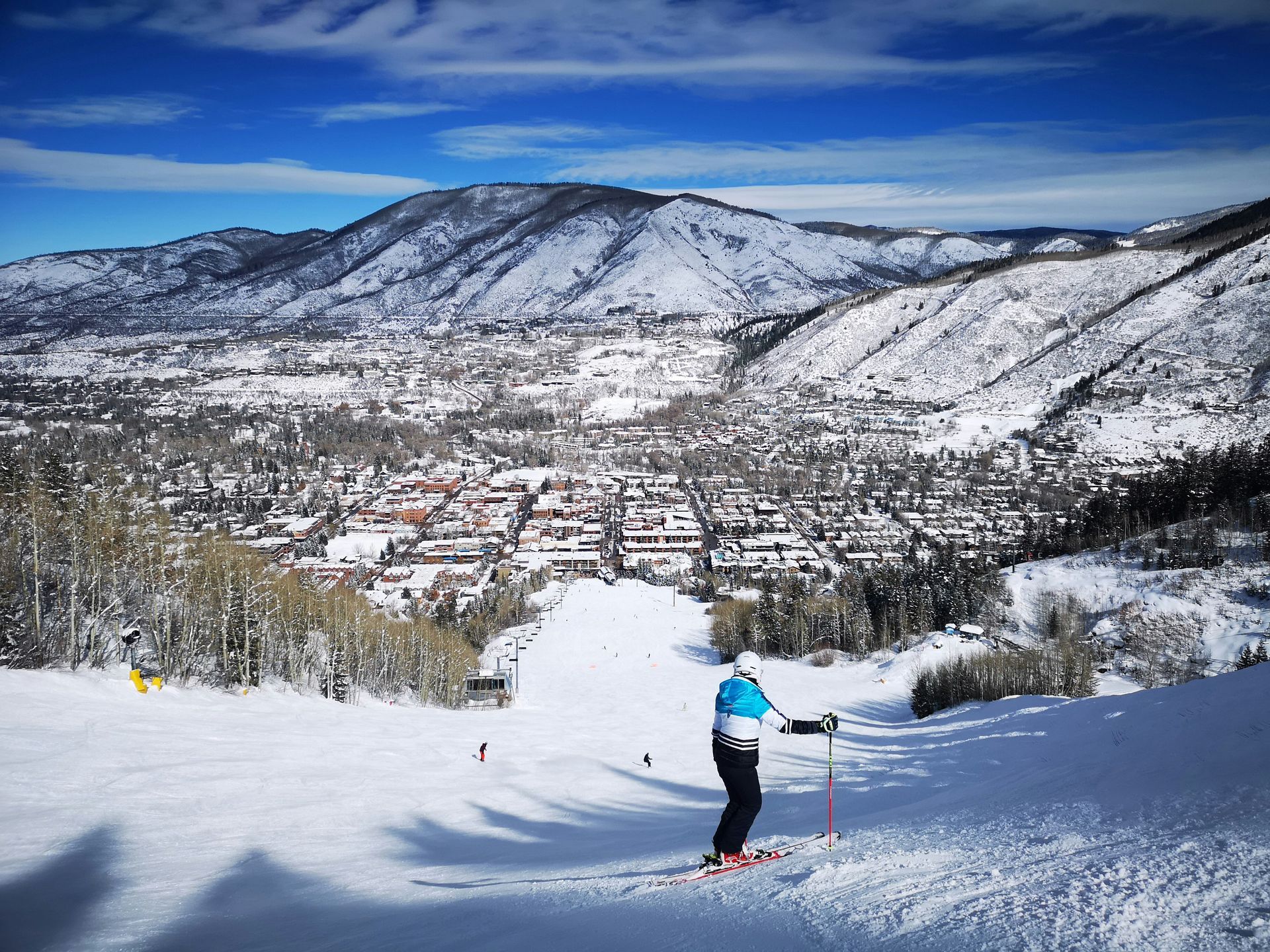 Skier on a snow-covered slope overlooking Aspen downtown on a bright, sunny day.
