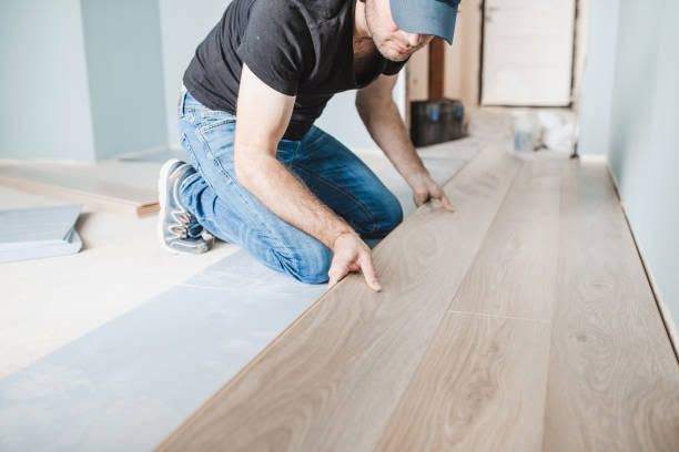 Person kneeling to install a light wood floor in a bright room