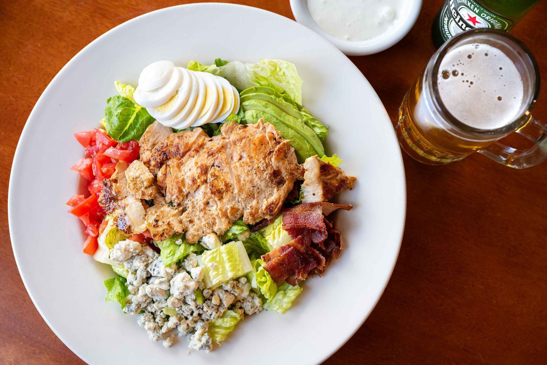 Plate of mixed food with rice, lettuce, tomato, egg, and meat beside a glass of beer on a wooden table