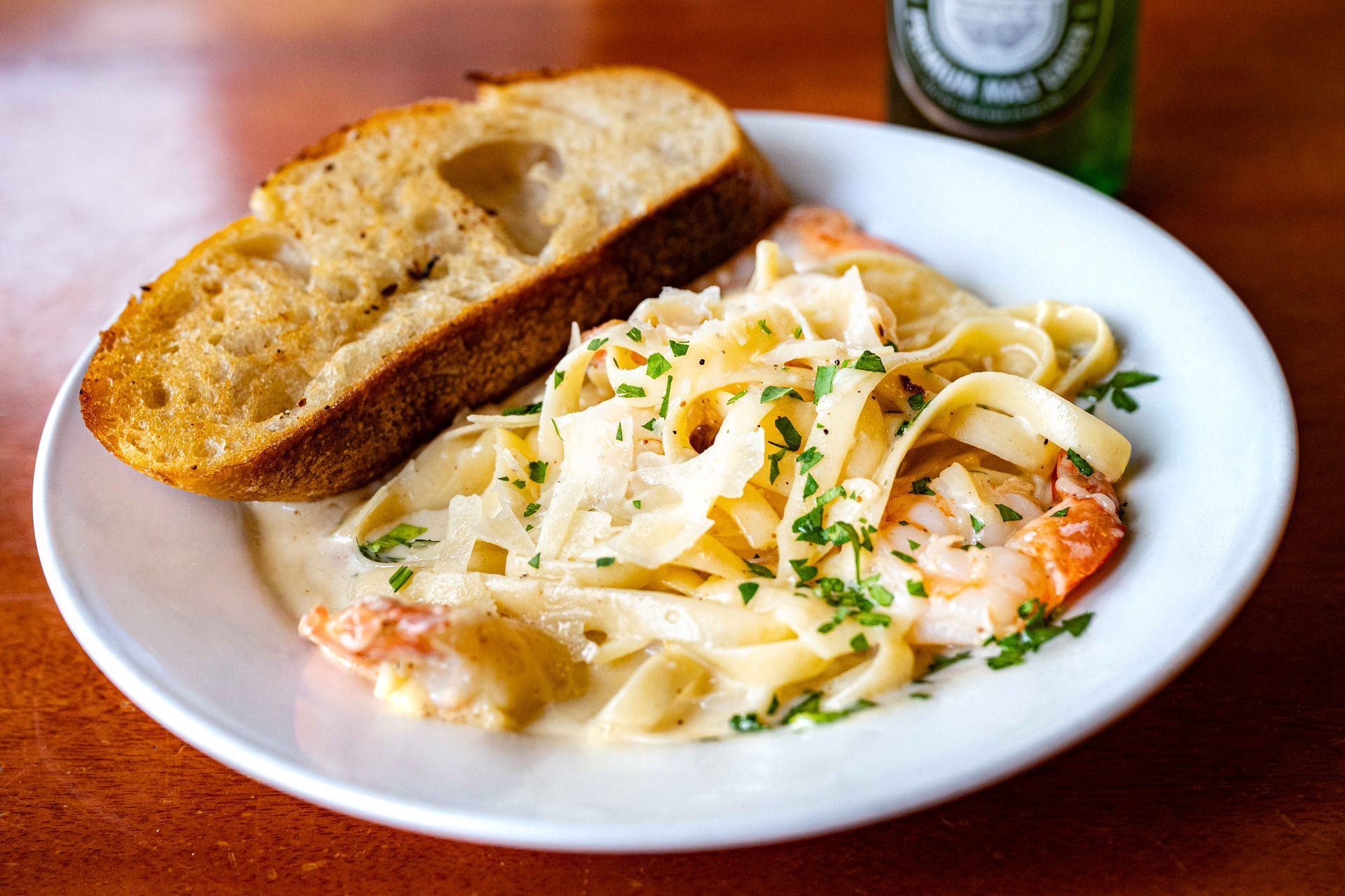 Plate of creamy pasta with shrimp and parsley, served with toasted bread on a white dish