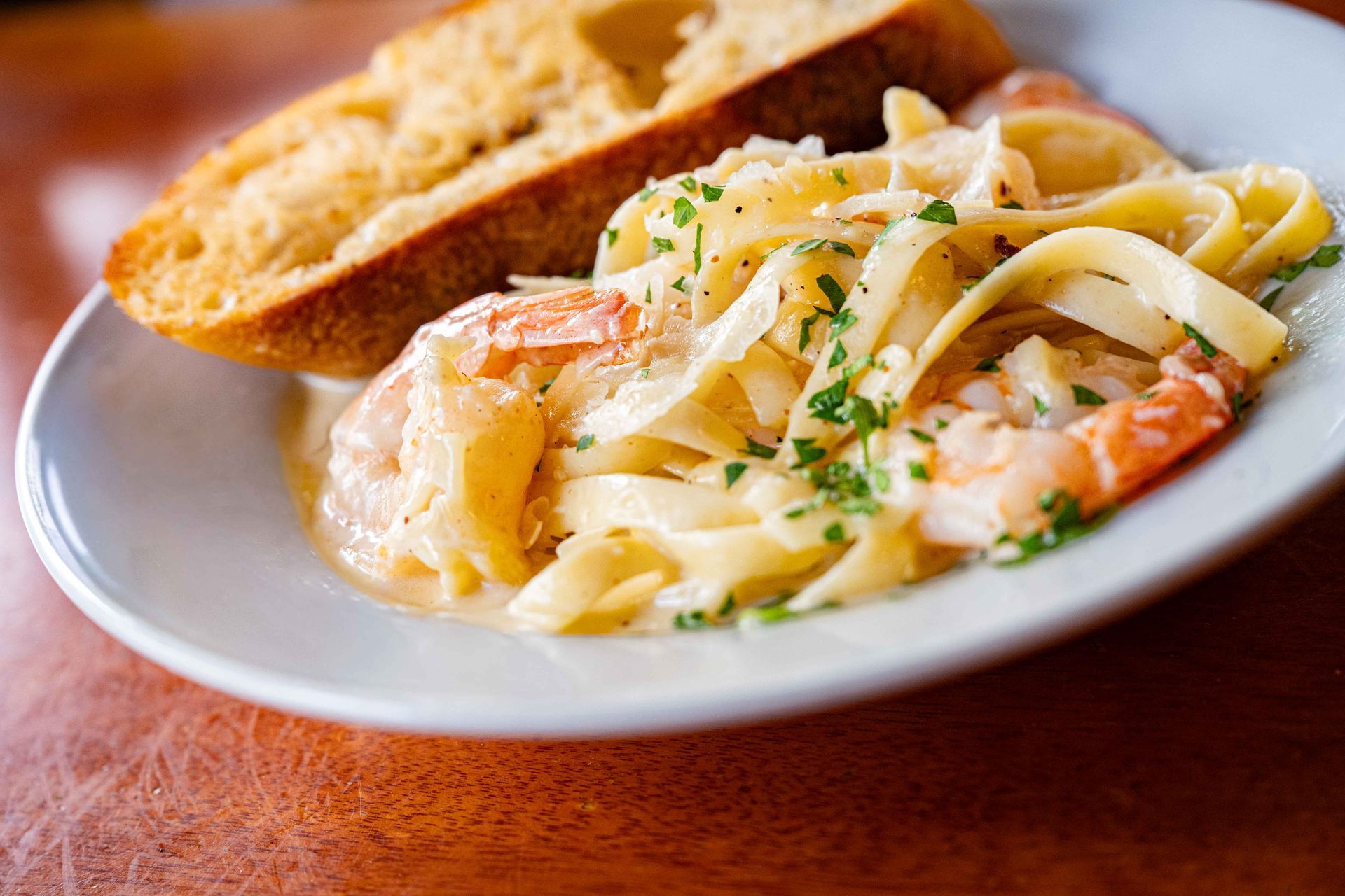 Plate of creamy pasta with shrimp and a slice of toasted bread on a wooden table