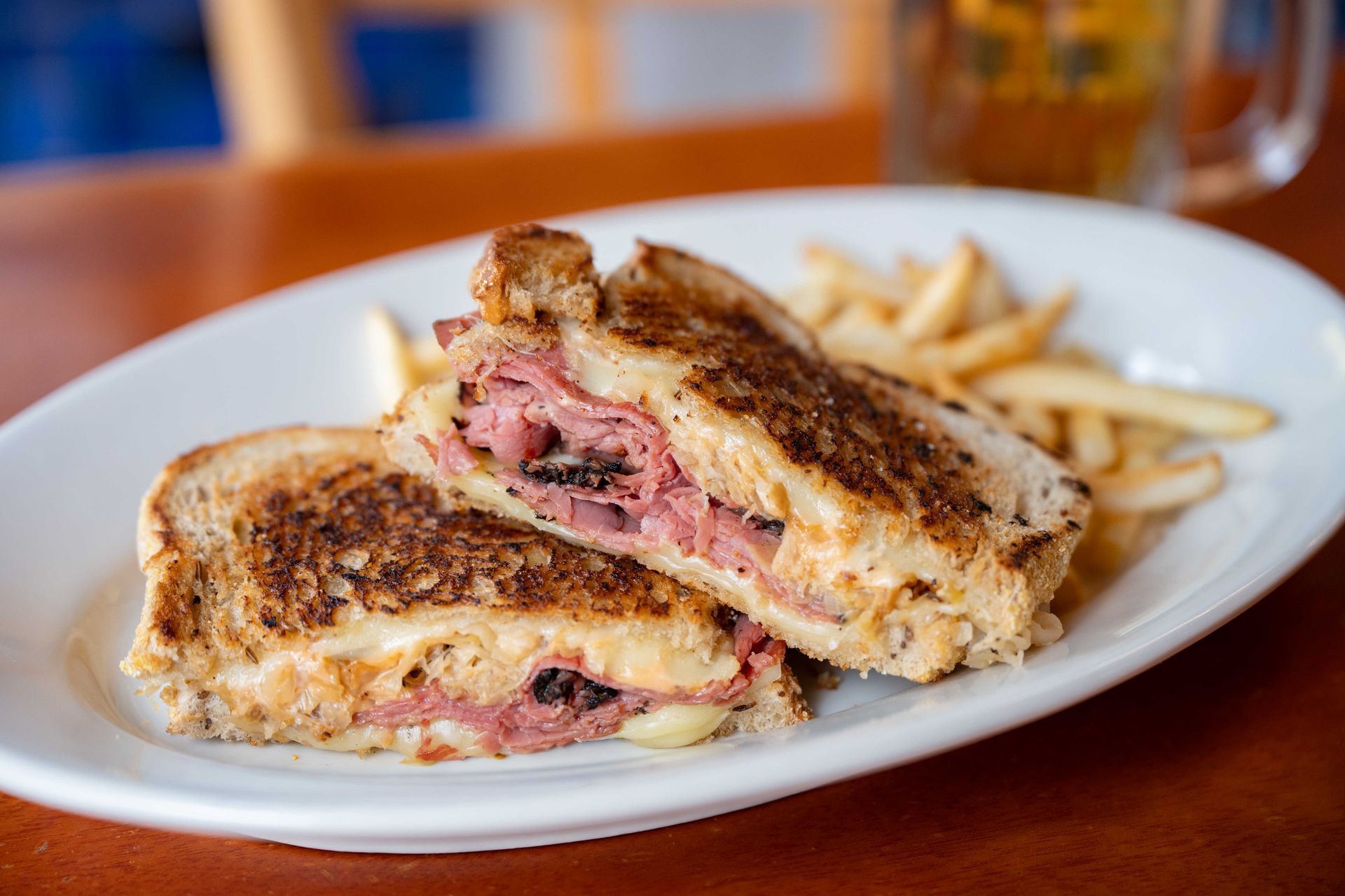 Grilled sandwich with melted cheese and ham on a white plate, with fries in the background