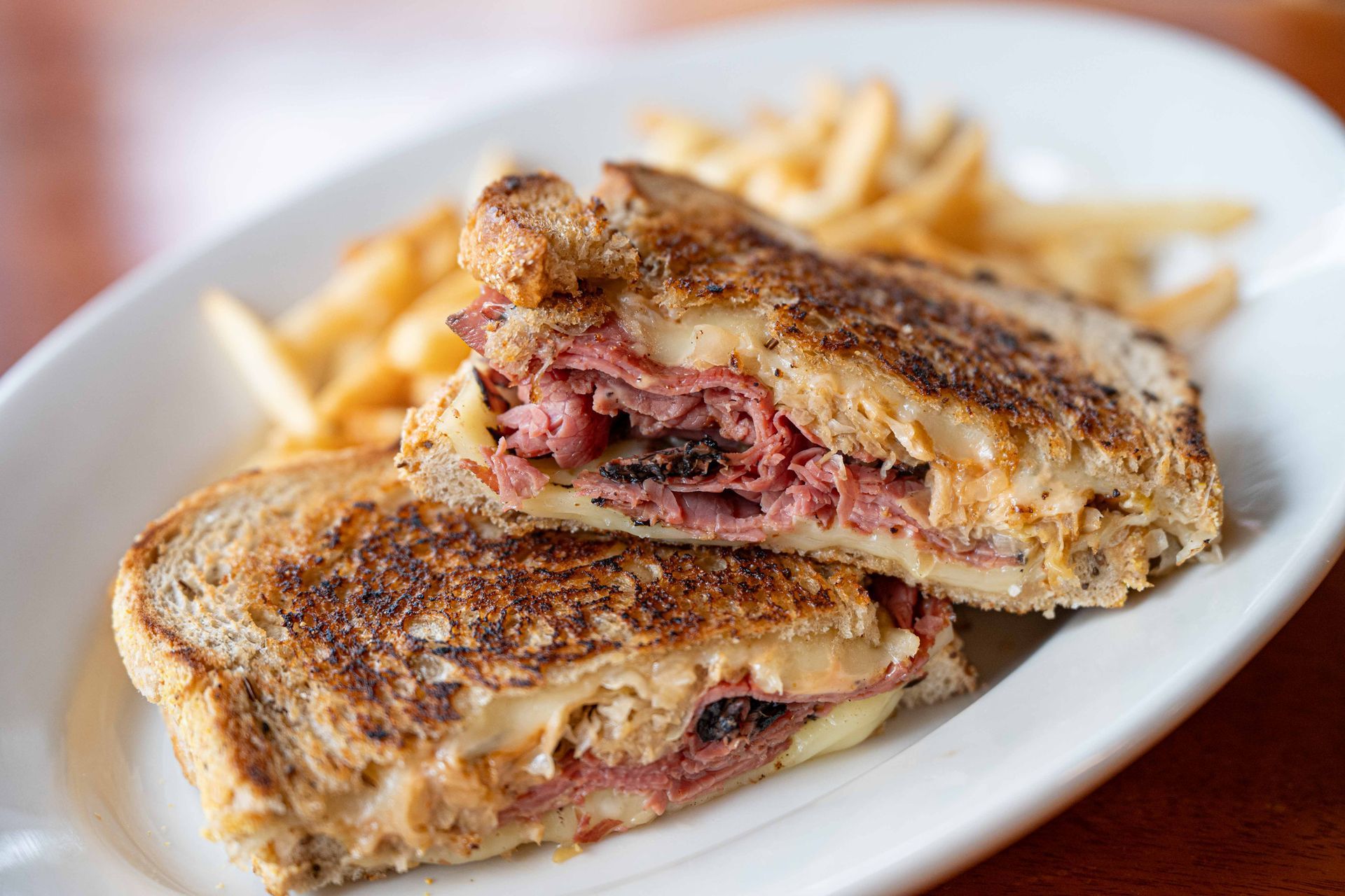 Grilled sandwich halves with melted filling on a white plate, with French fries in the background