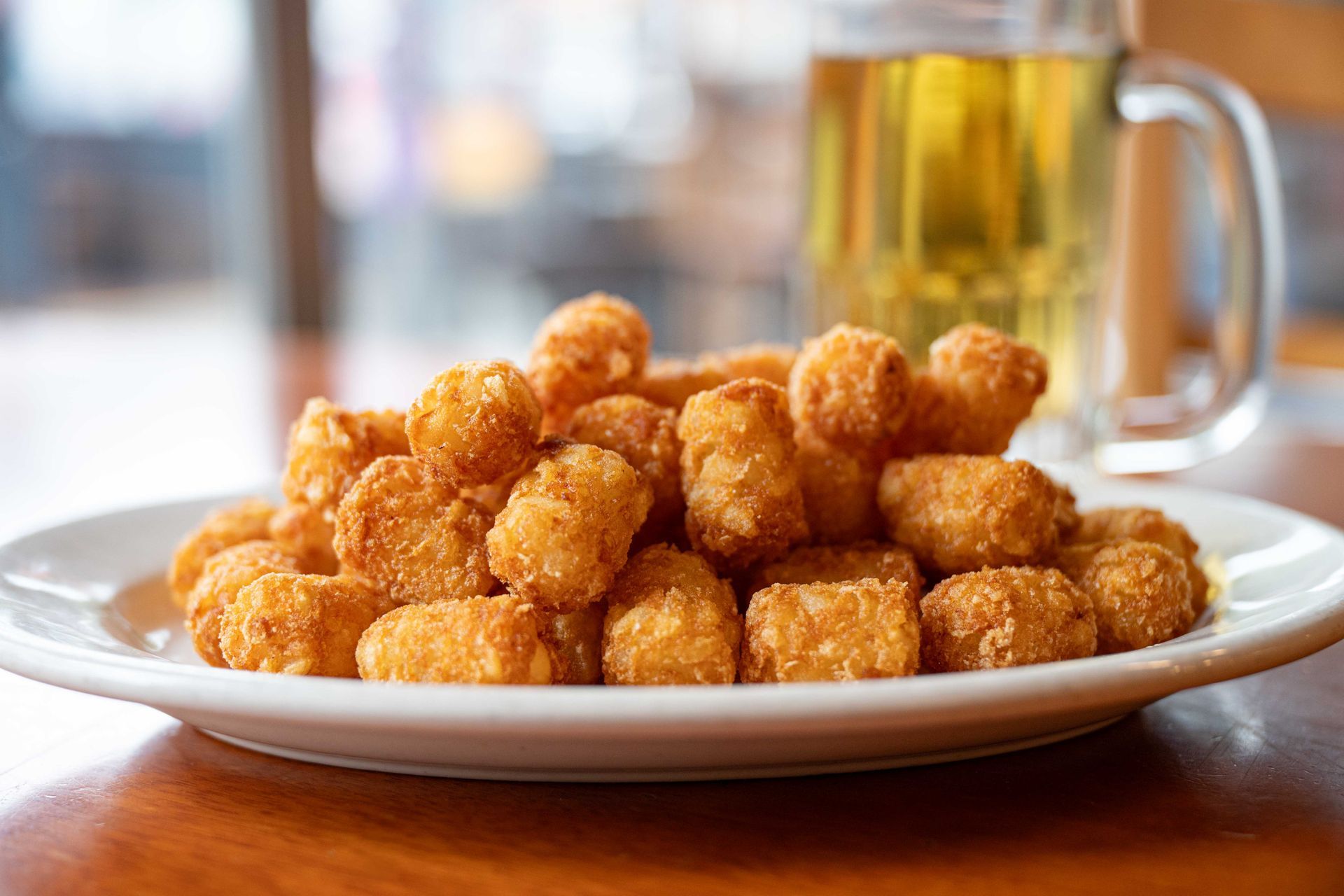 Plate of golden fried snack bites beside a glass mug of beer on a wooden table