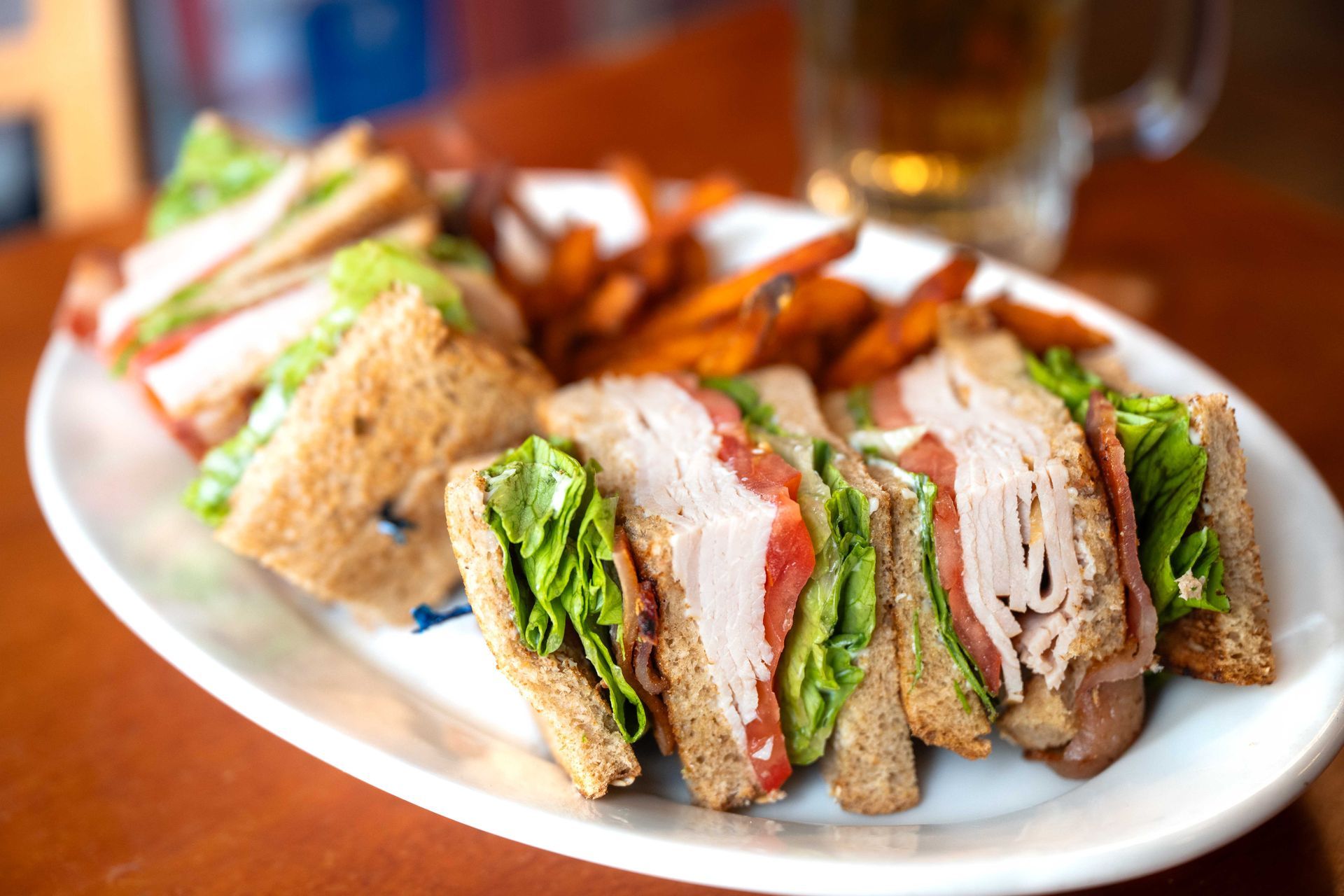 Sandwich halves on a white plate, filled with lettuce, tomato, and meat on a wooden table