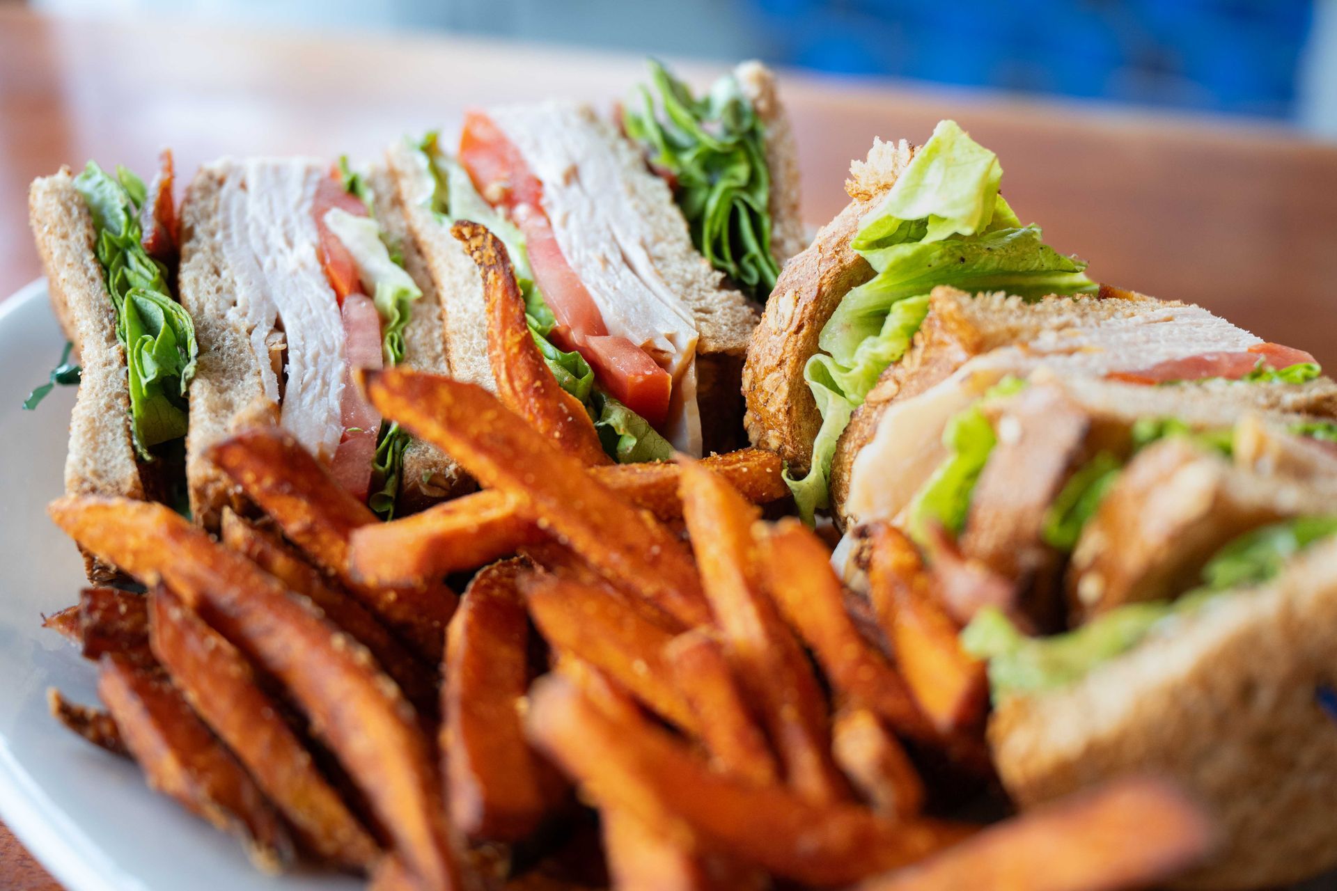 Sandwich with fries on a plate, stacked with lettuce, tomato, and sliced meat.