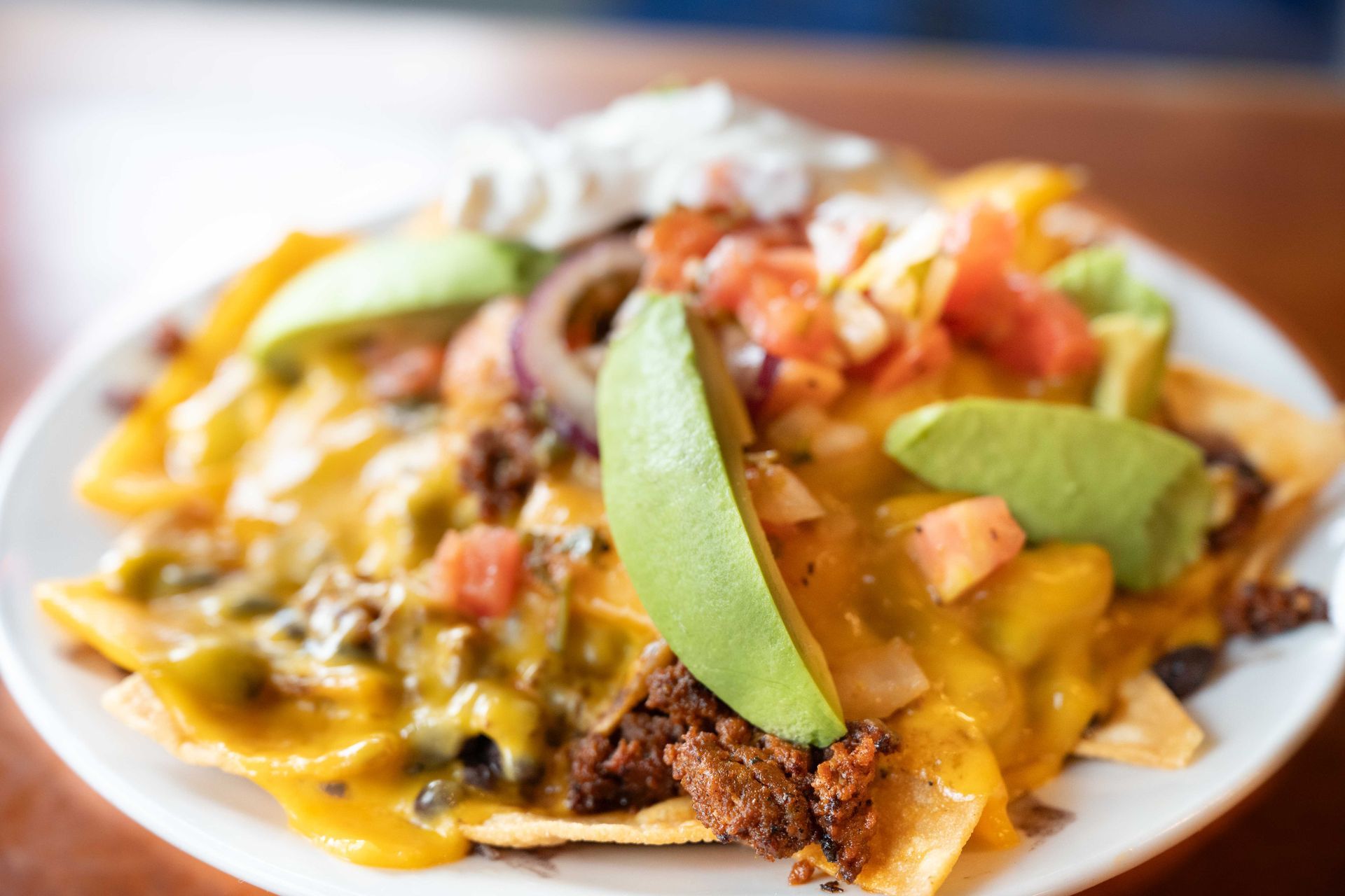 Plate of nachos topped with avocado slices, cheese, salsa, and sour cream on a table